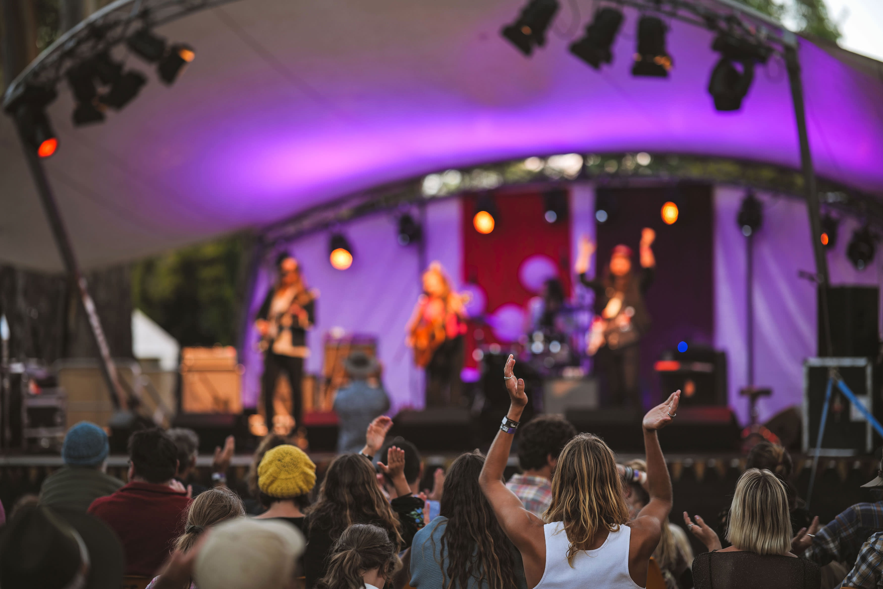A purple stage in the background with live band, with crowd facing in the foreground