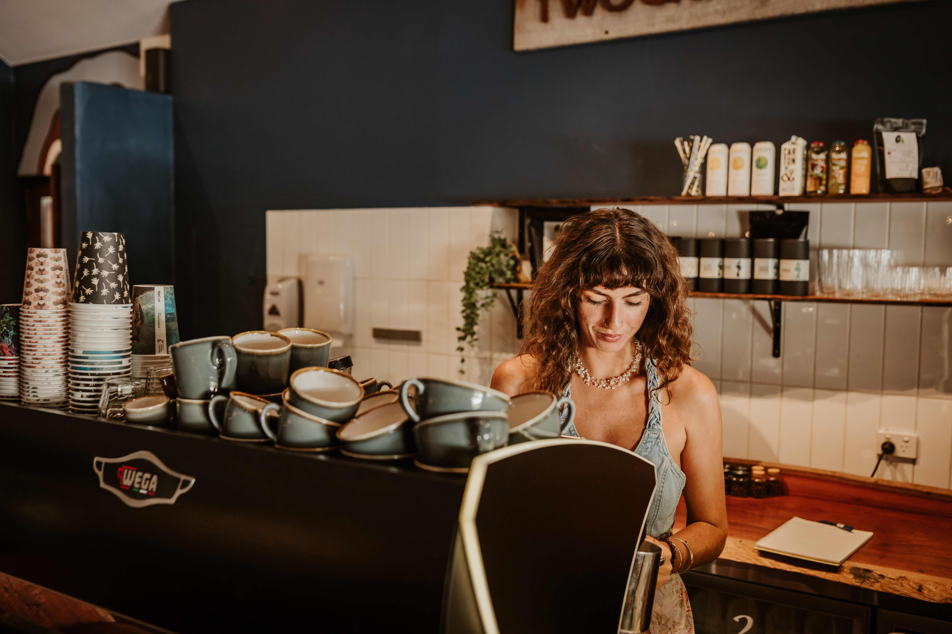 A lady barista with brown hair standing behind a coffee machine