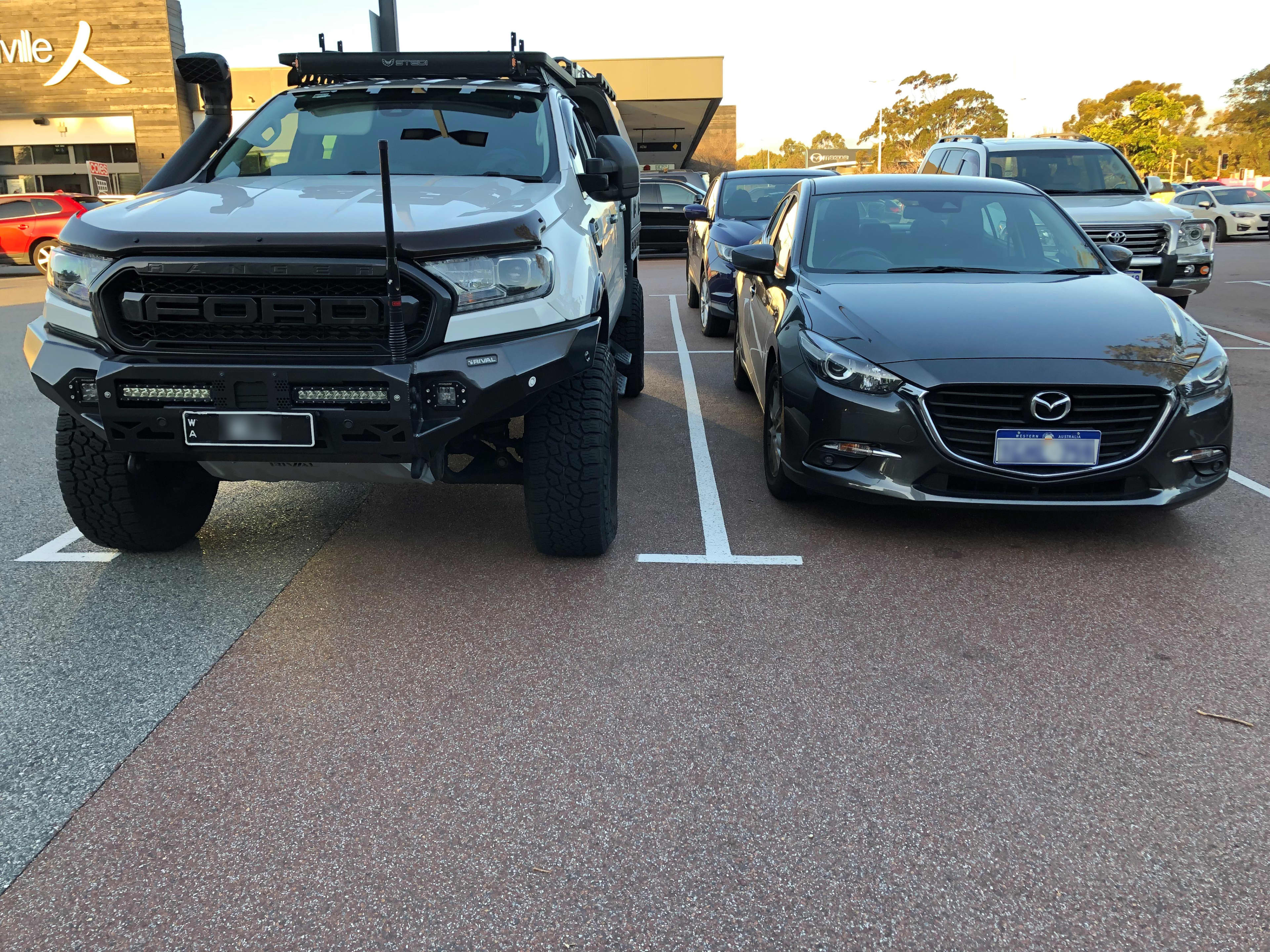 A white Ford Ranger next to a black Mazda 3 in a car park.