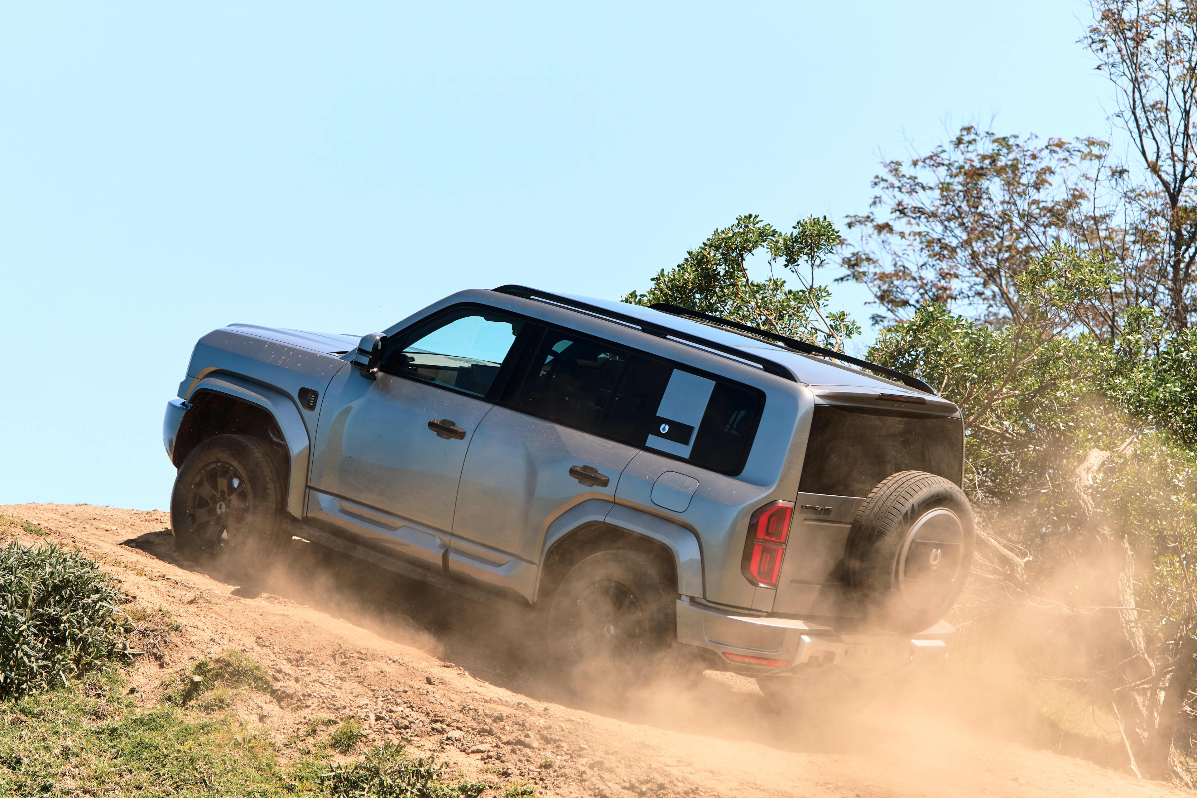 A light grey BYD Denza driving up a sandy embankment