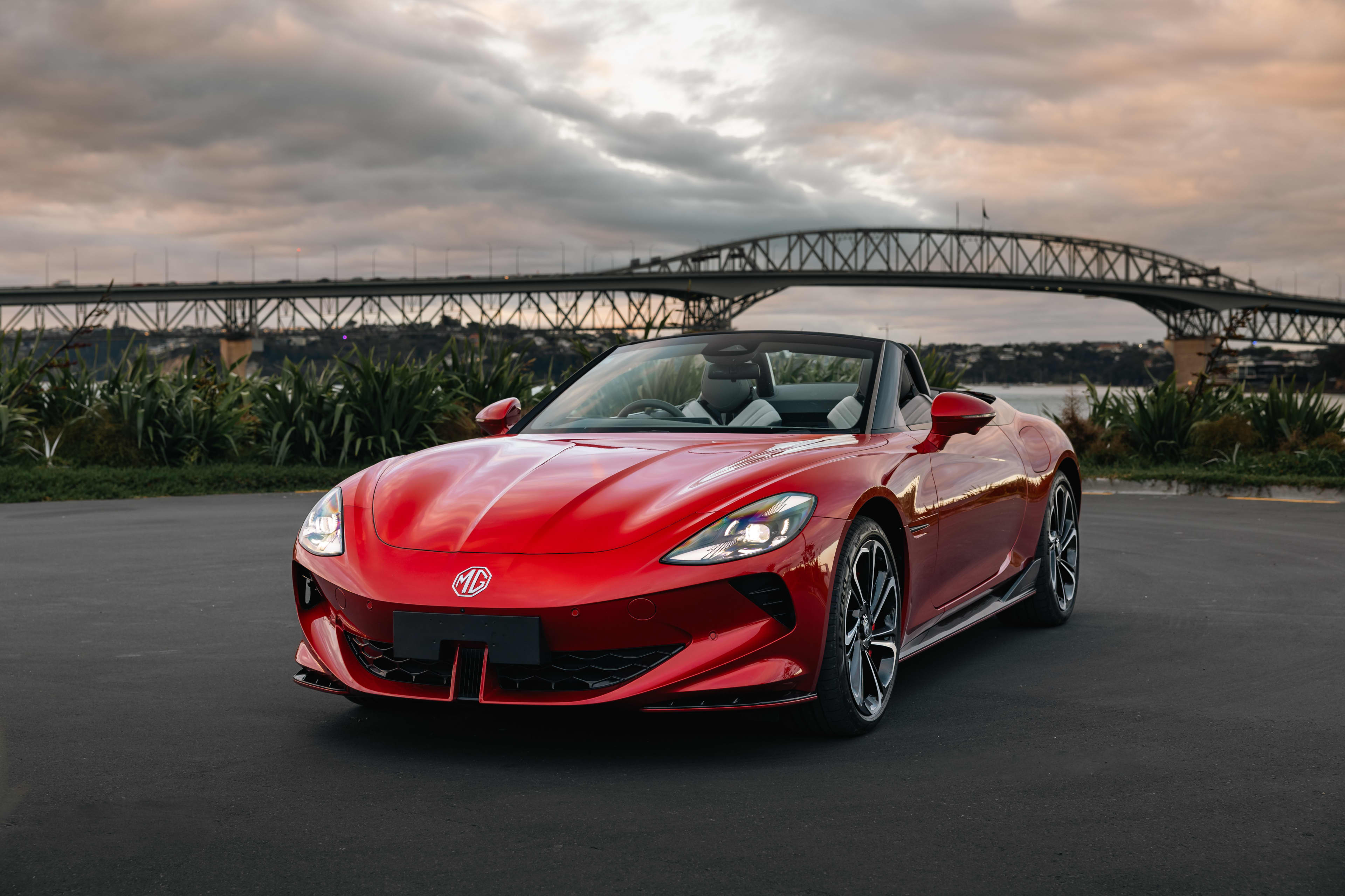 A red MG Cyberster parked on tarmac near a bridge