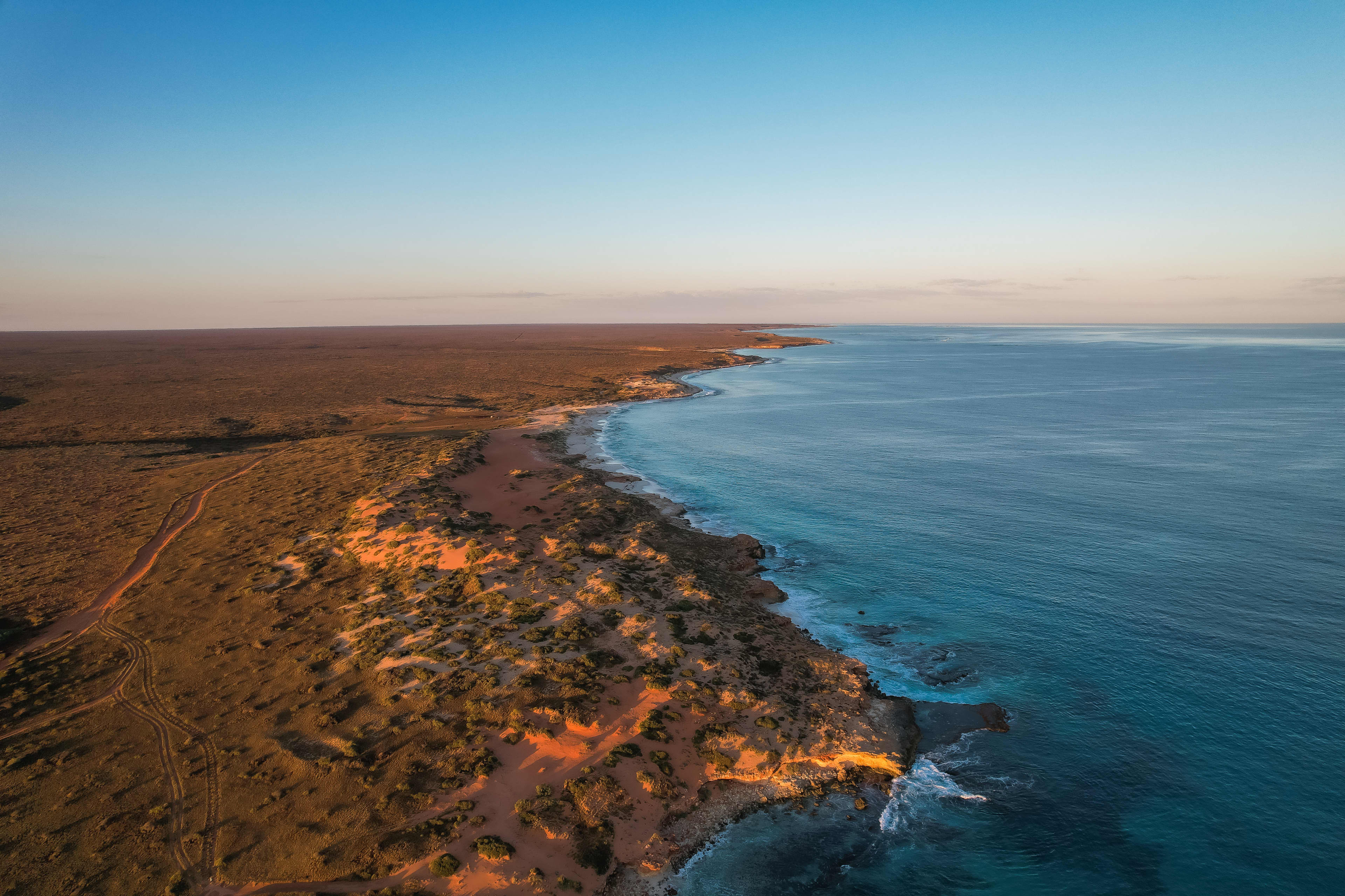 An aerial shot of red dirt sand meeting the ocean during sunset.