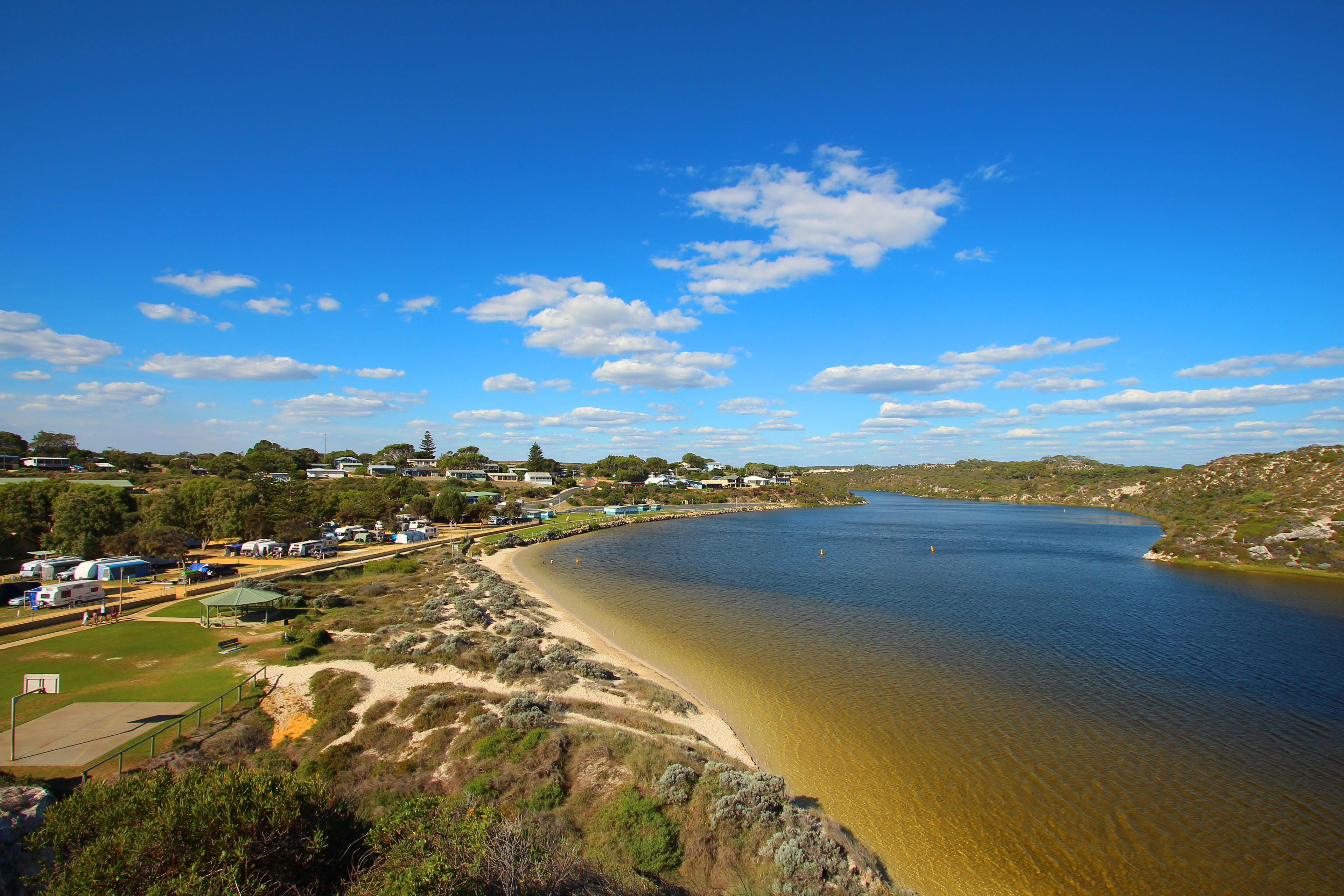 A scenic estuary running through a town with campers and caravans parked on the nearby grass