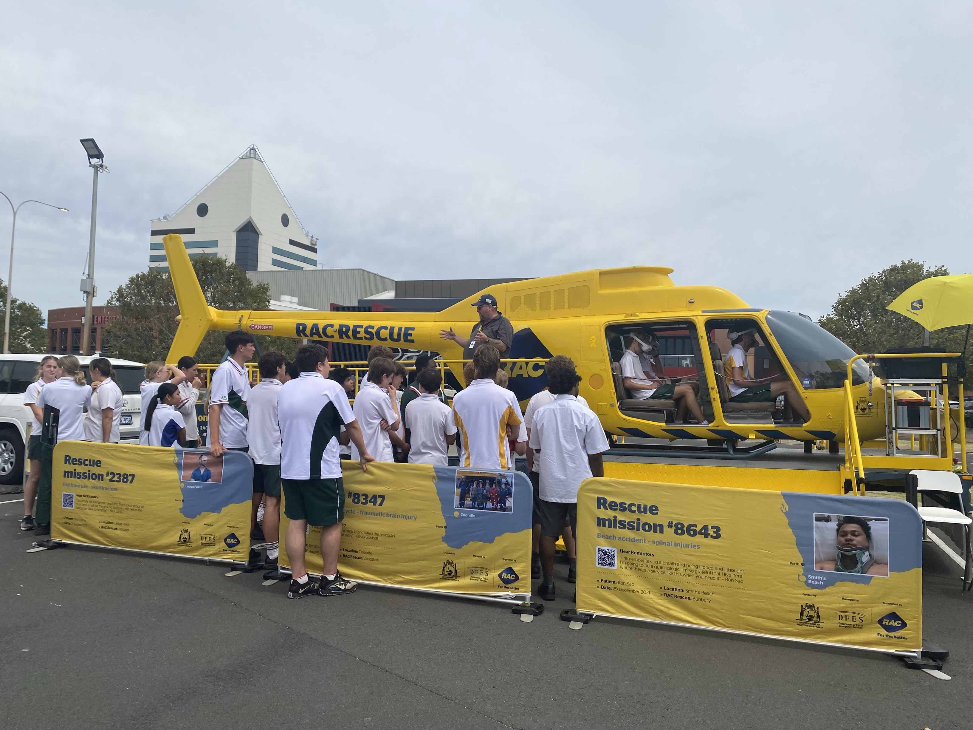 Students standing around the yellow RAC rescue helicopter while a presenter speaks.