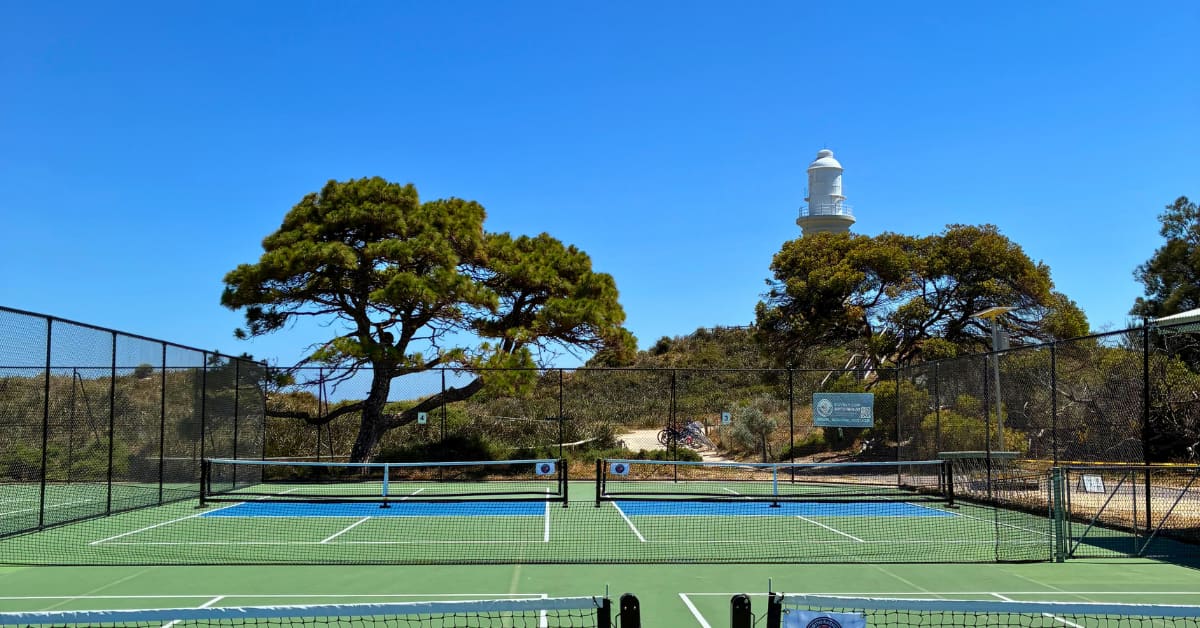 Green pickleball courts in bush setting with lighthouse in background