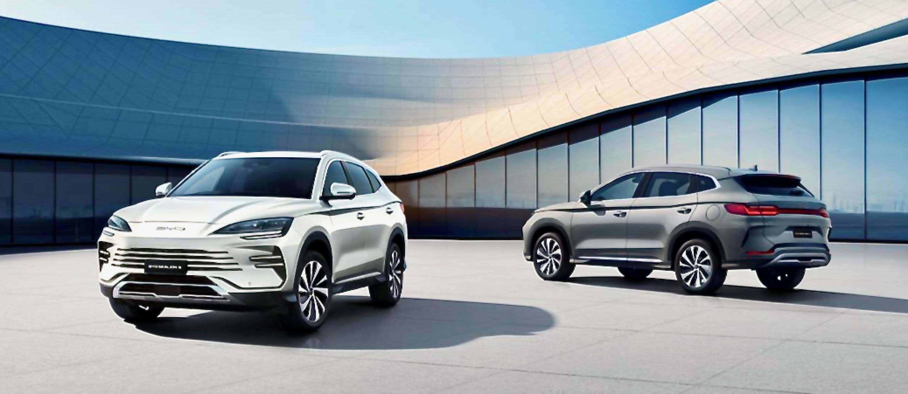 A white and a silver BYD Sealion parked in front of a modern building