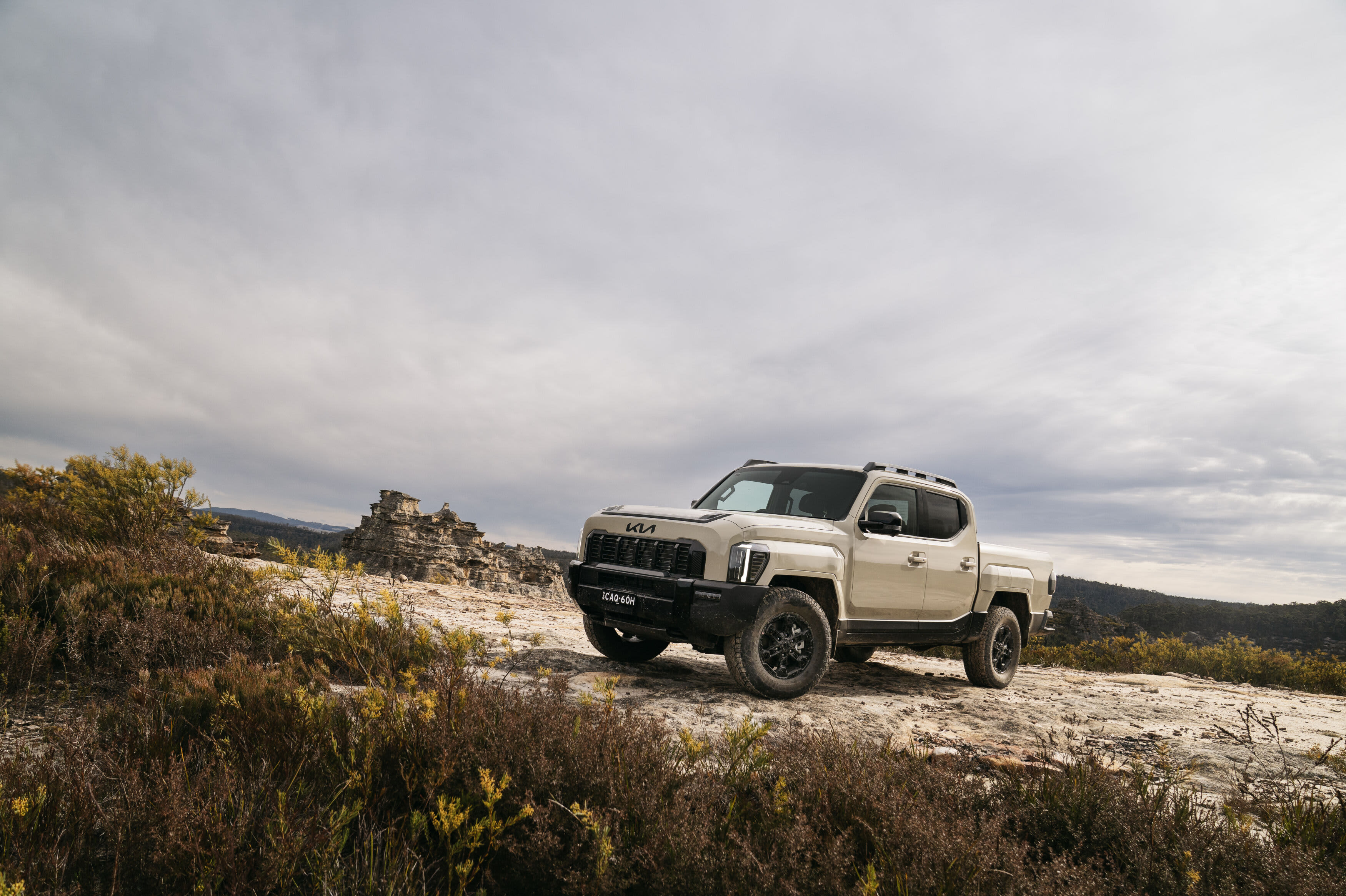 A light brown Kia Tasman ute parked on a rocky hillside