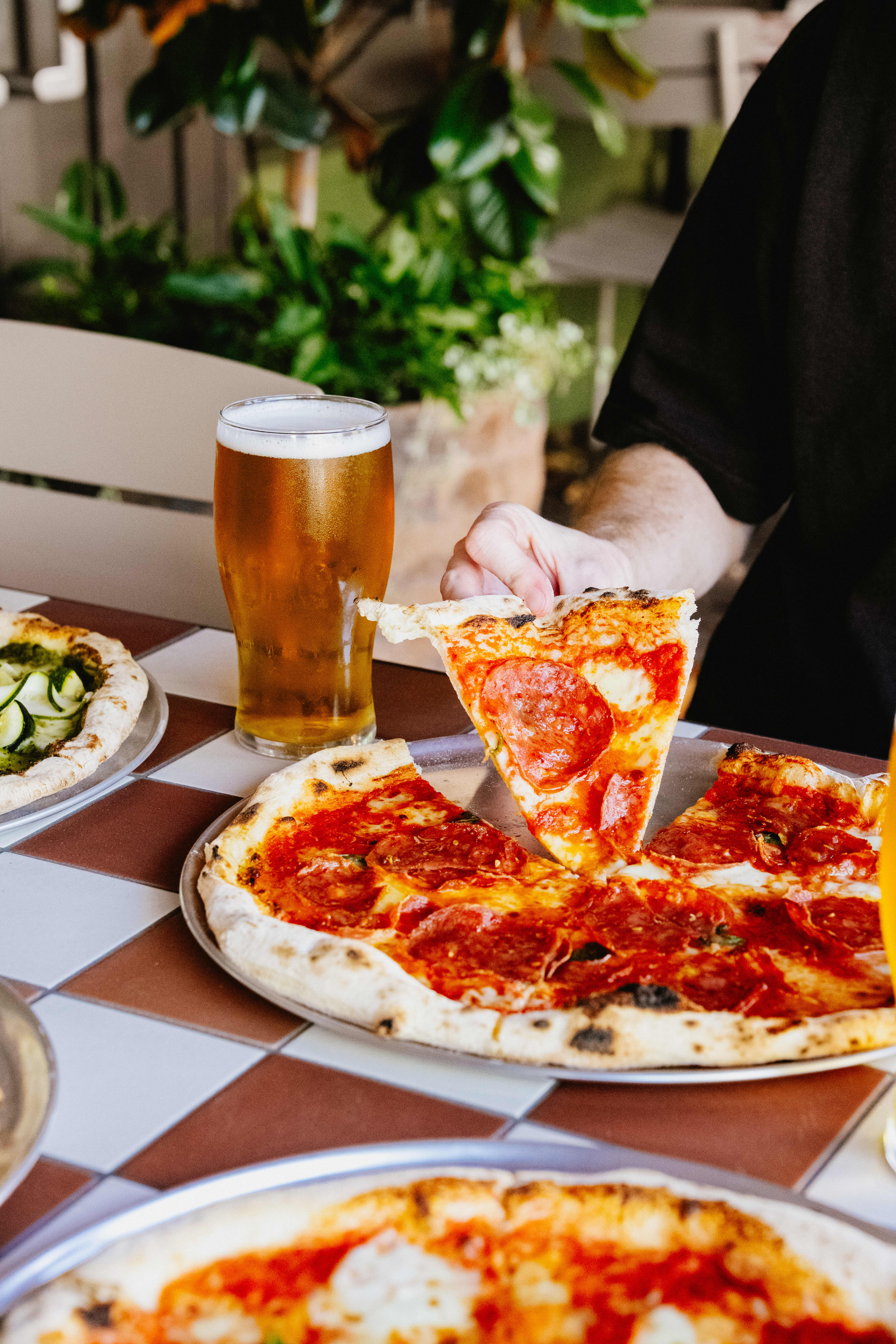 Slices of pizza being eaten outdoors in garden seating accompanied by a beverage