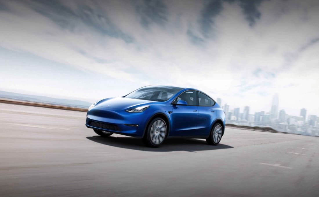 A blue Tesla Model Y driving on a highway against a city backdrop