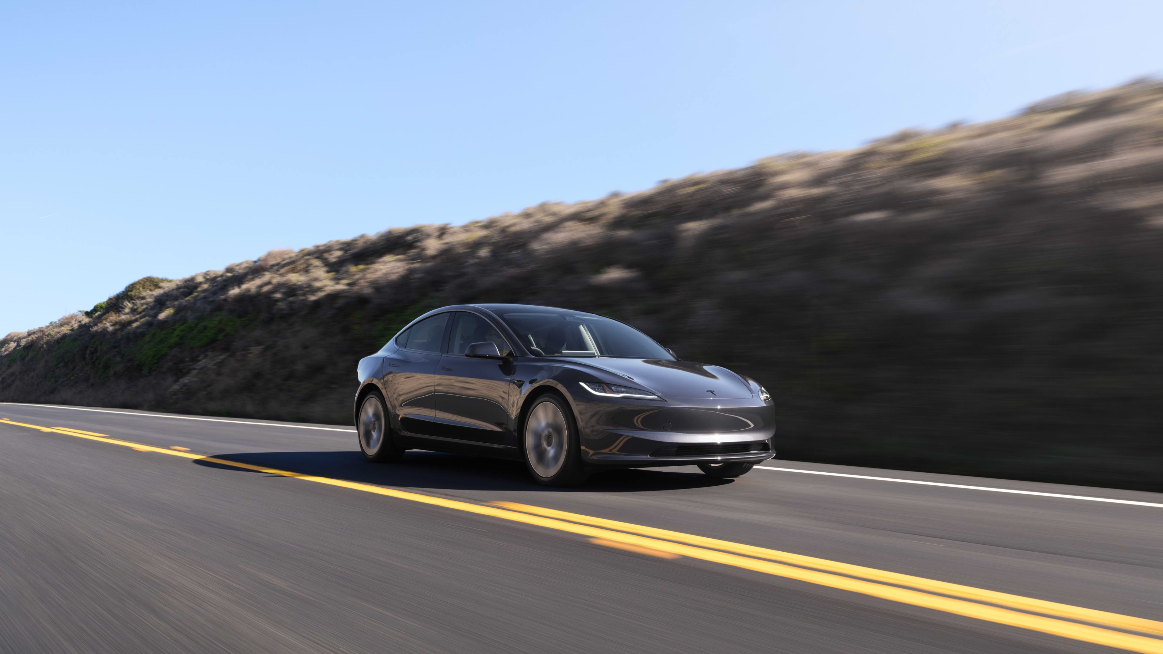 A dark grey Tesla Model 3 driving on a country road