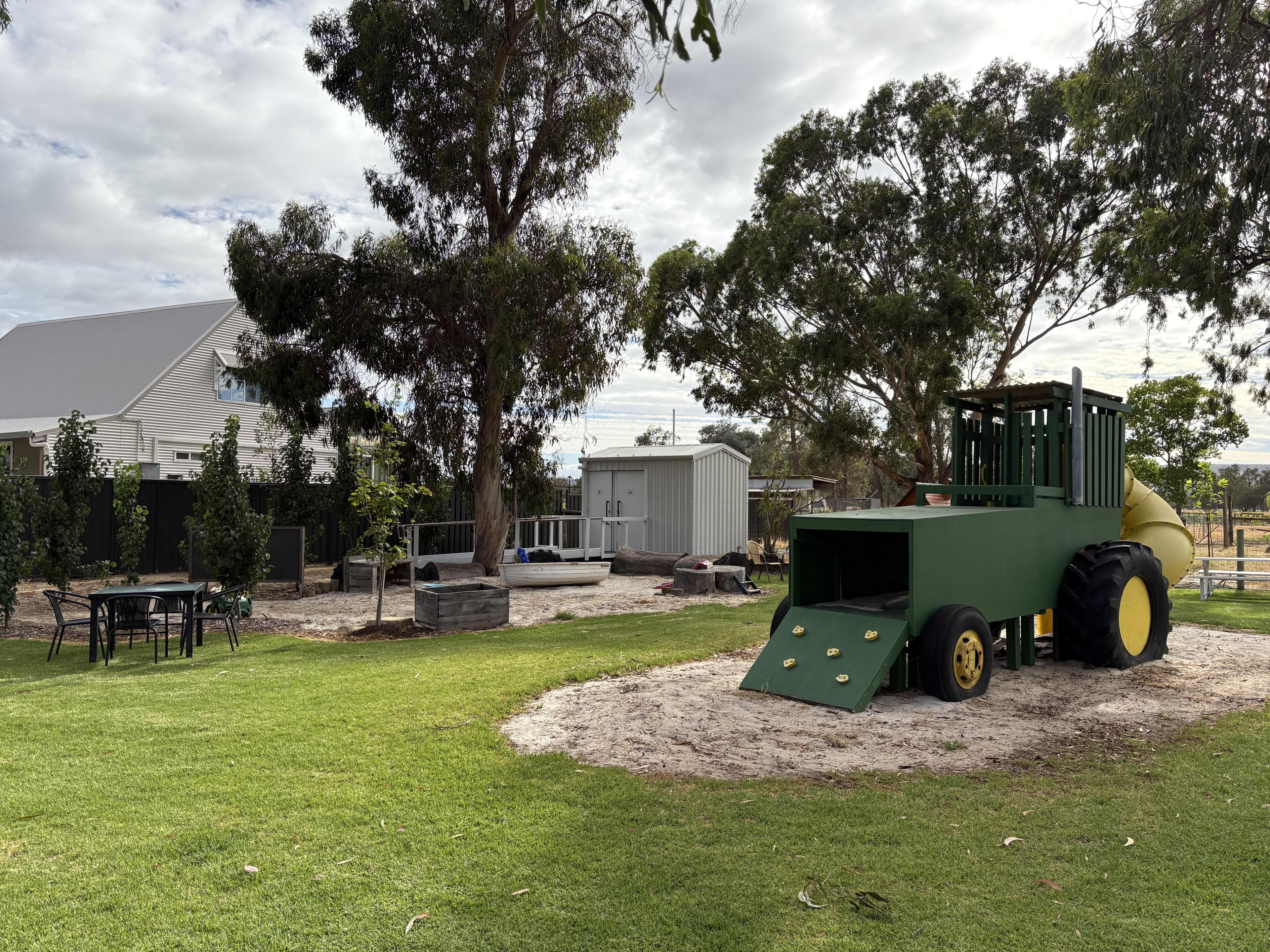 A lush lawn with a large John Deer tractor inspired playset for children.