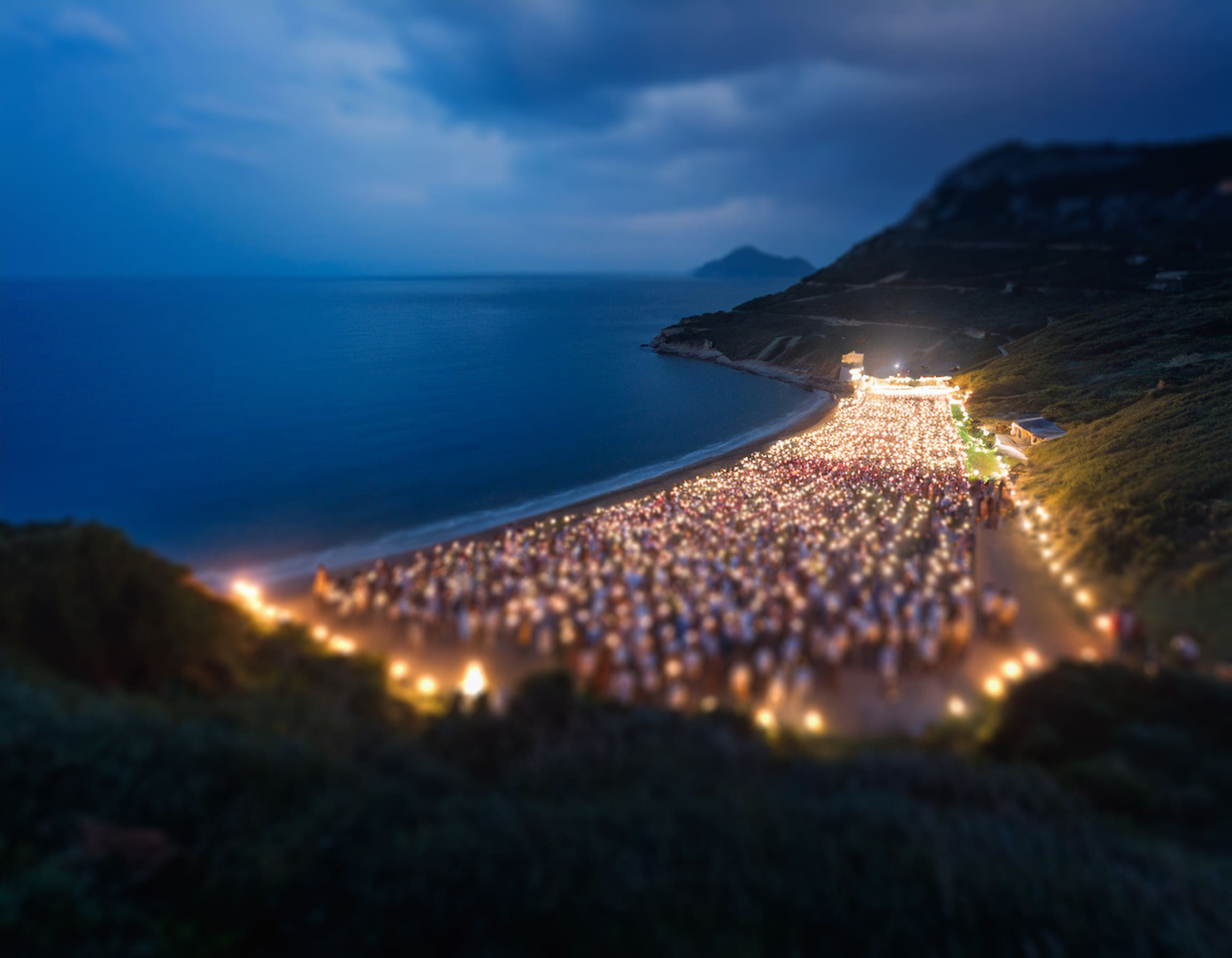 Aerial view of two mountains with lights lining the beach between them and the ocean outstretched