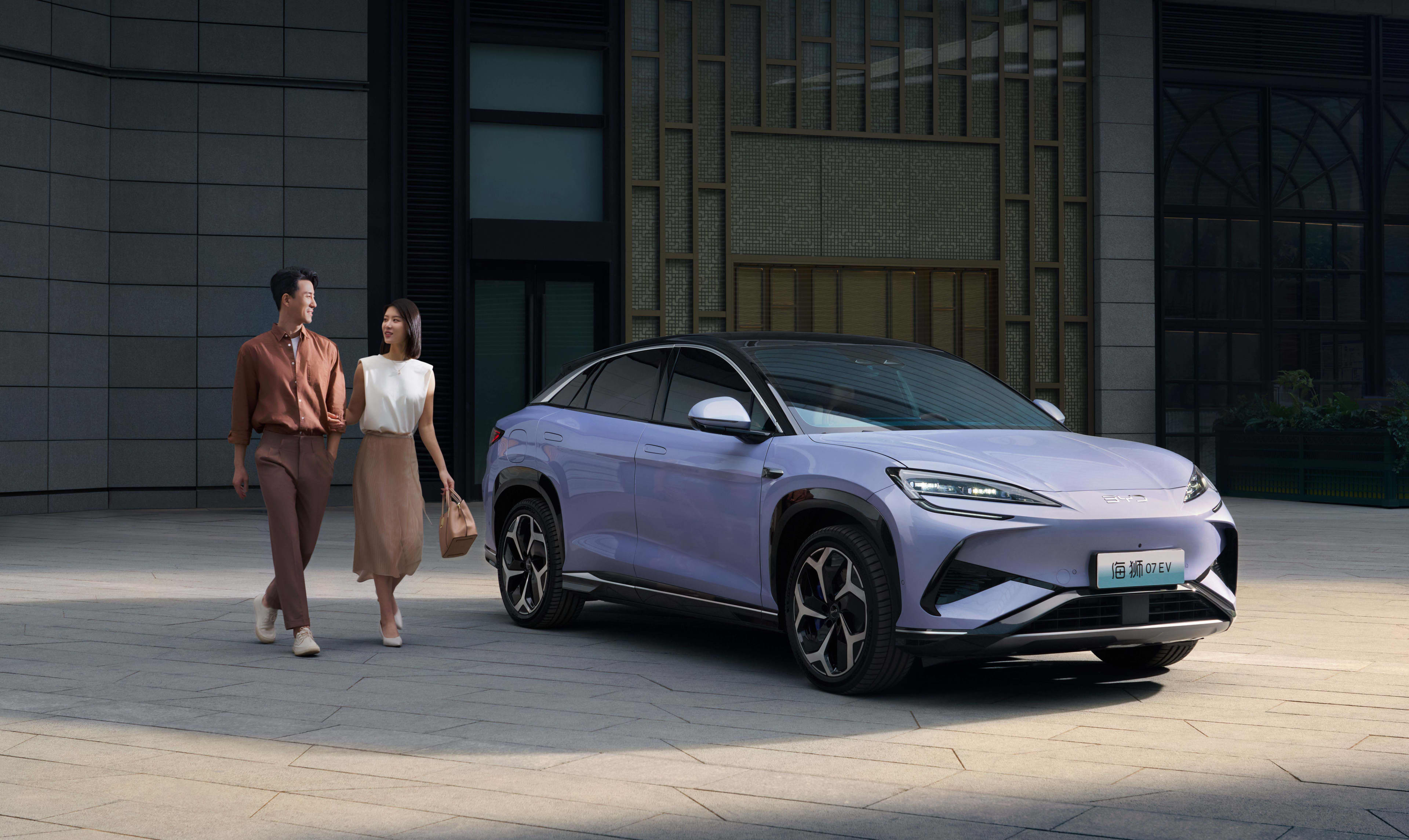 A purple BYD Sealion parked in a city square with 2 people walking by