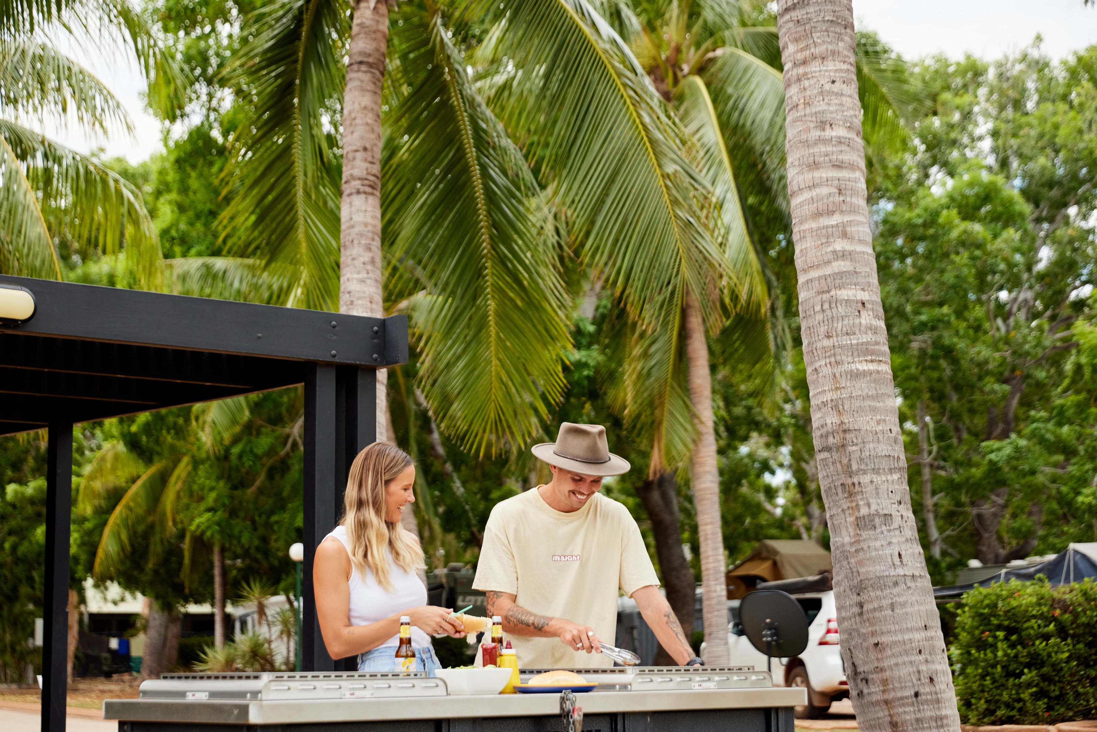 Two people at a BBQ with palm trees in the background