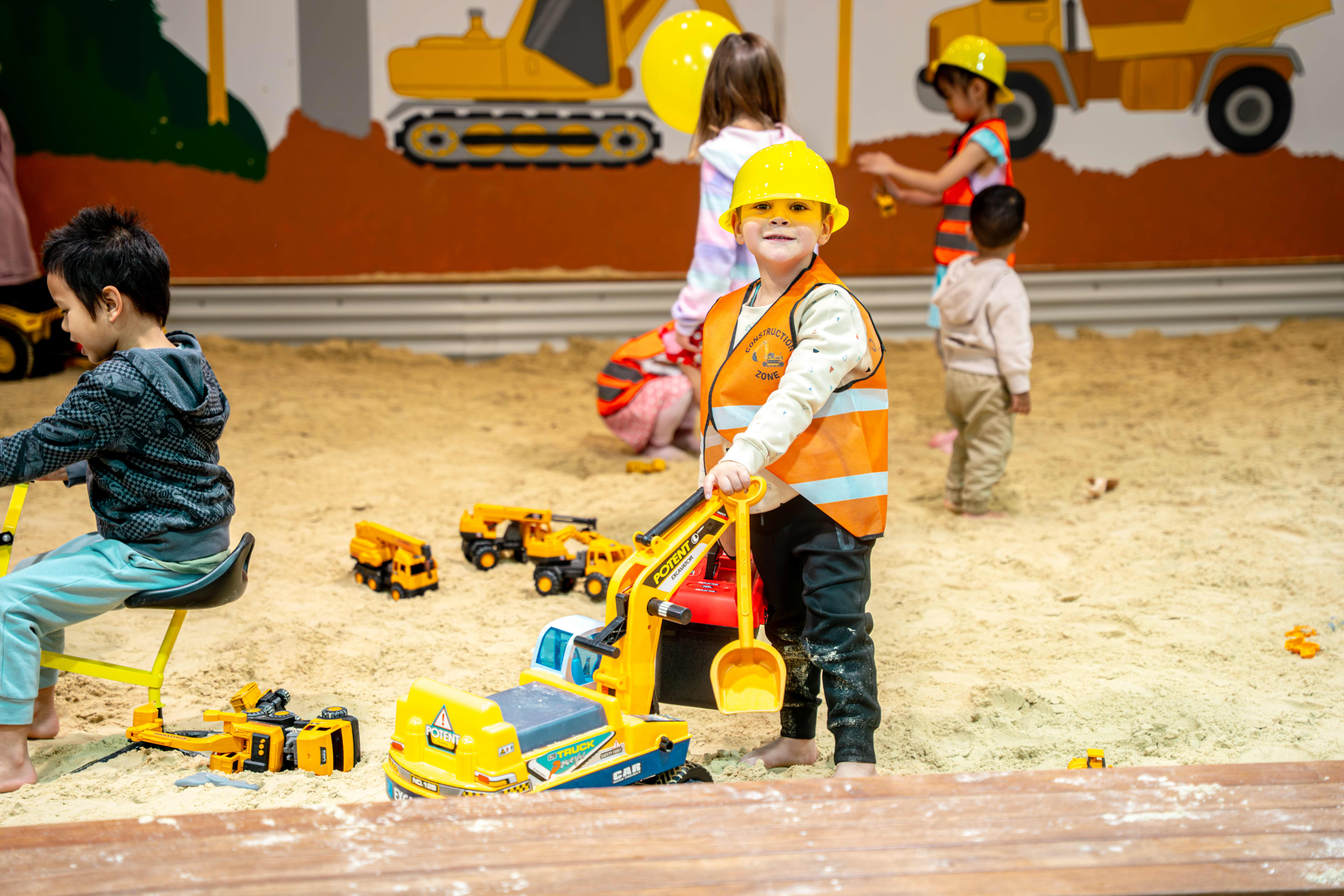 Children playing in large sandpit with construction toys