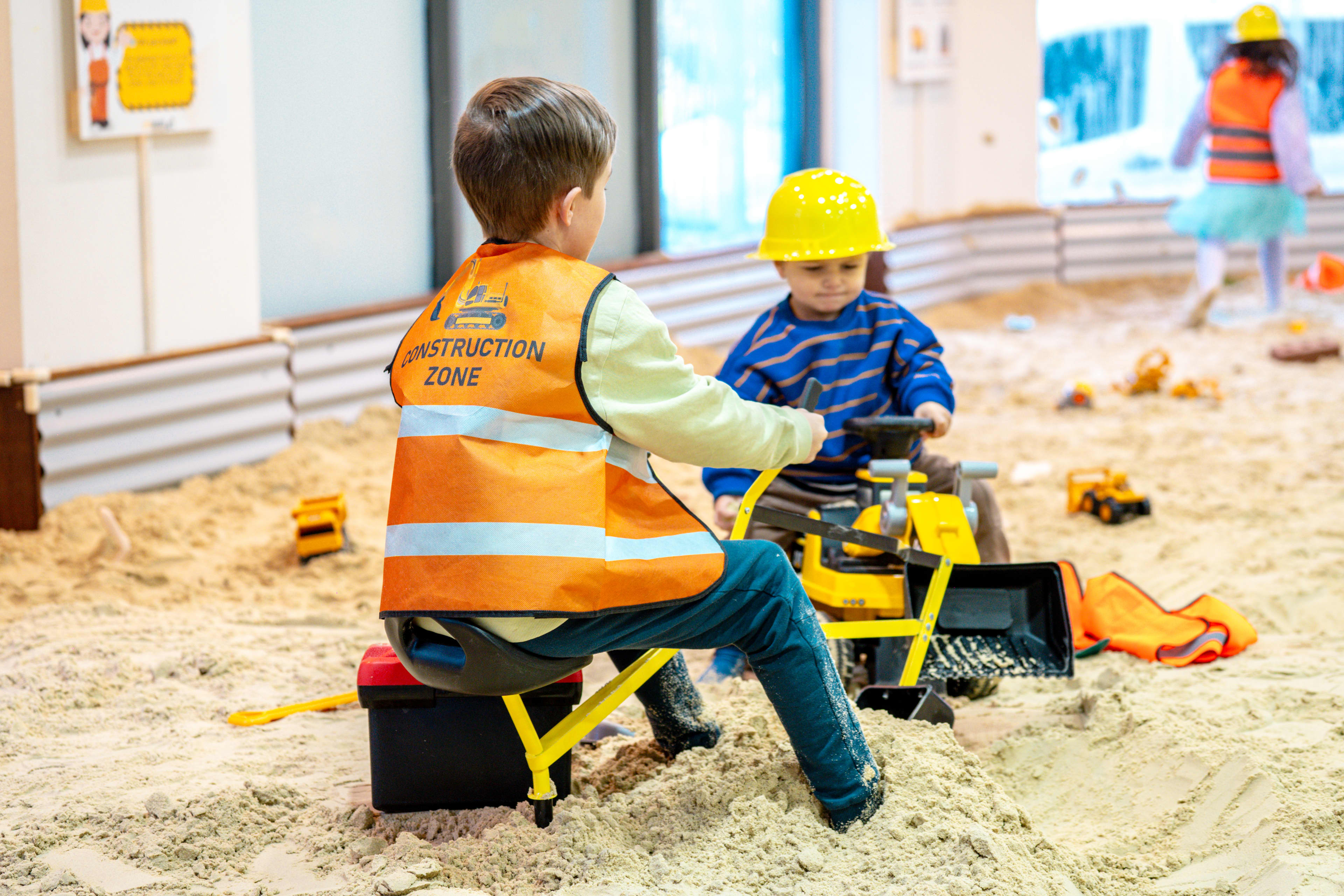 Young children in high-vis gear playing with toys in construction play sandpit