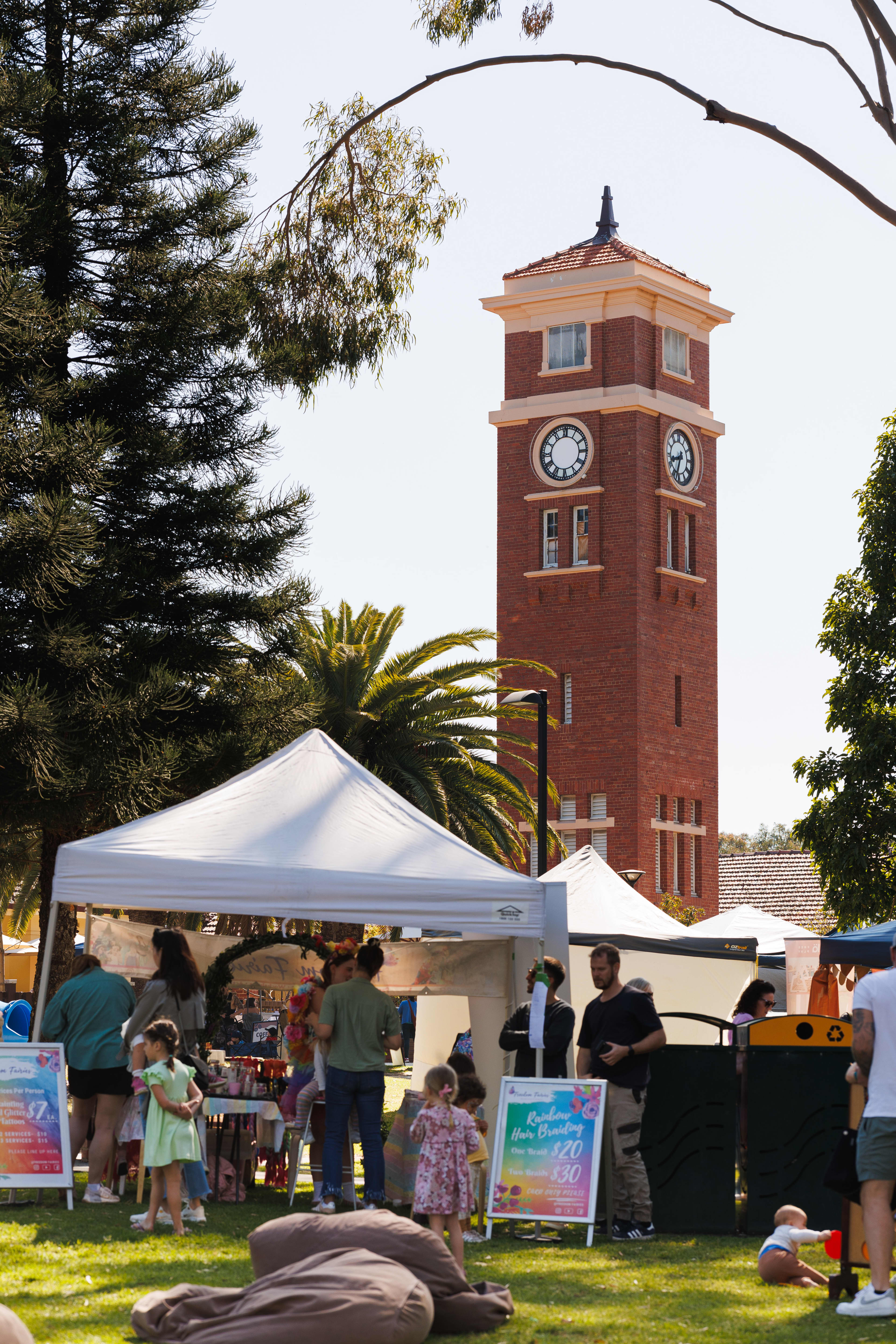 Market stalls in front of old tower surrounded by trees