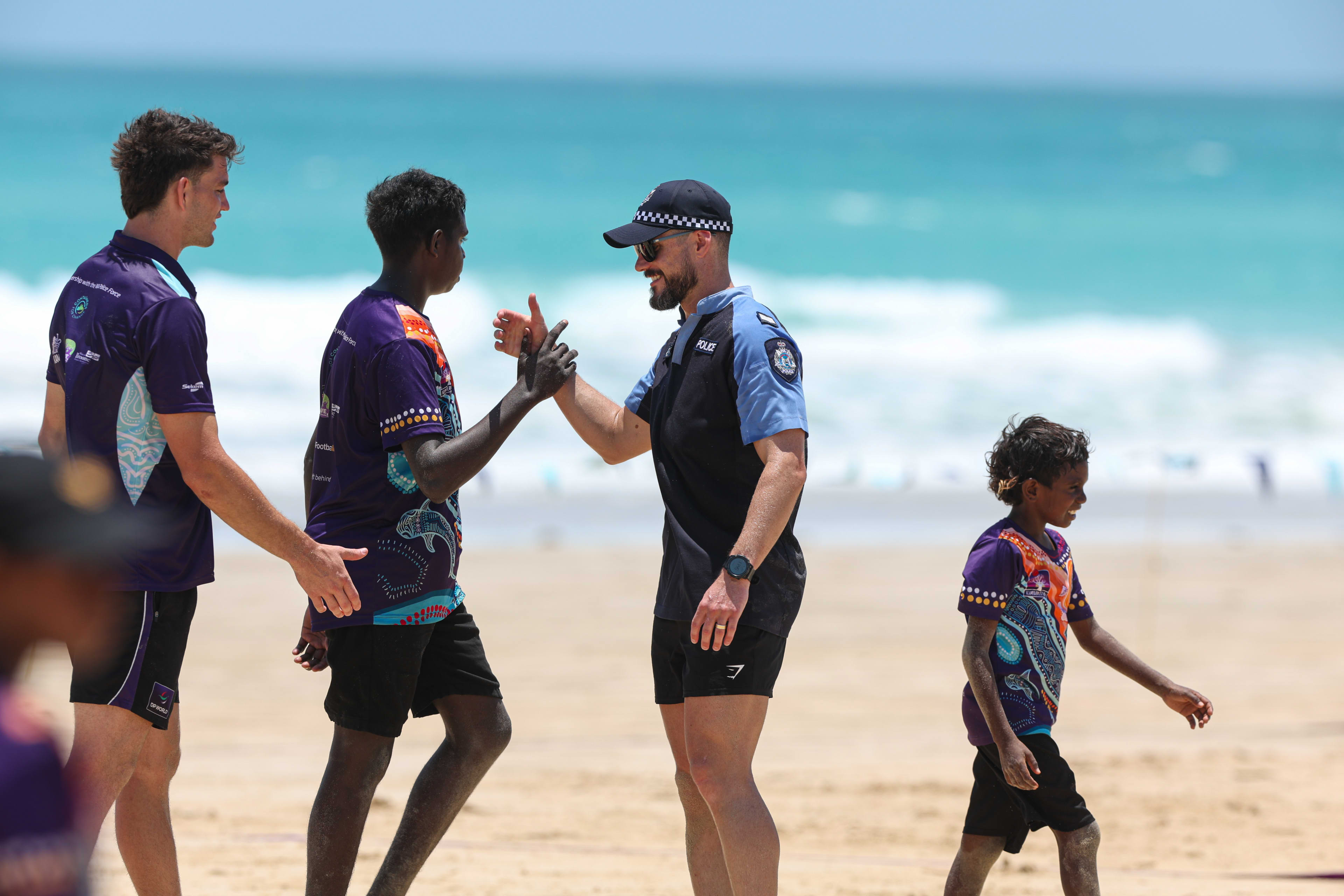 Students clasping hands with police officer on the beach after a game of football.