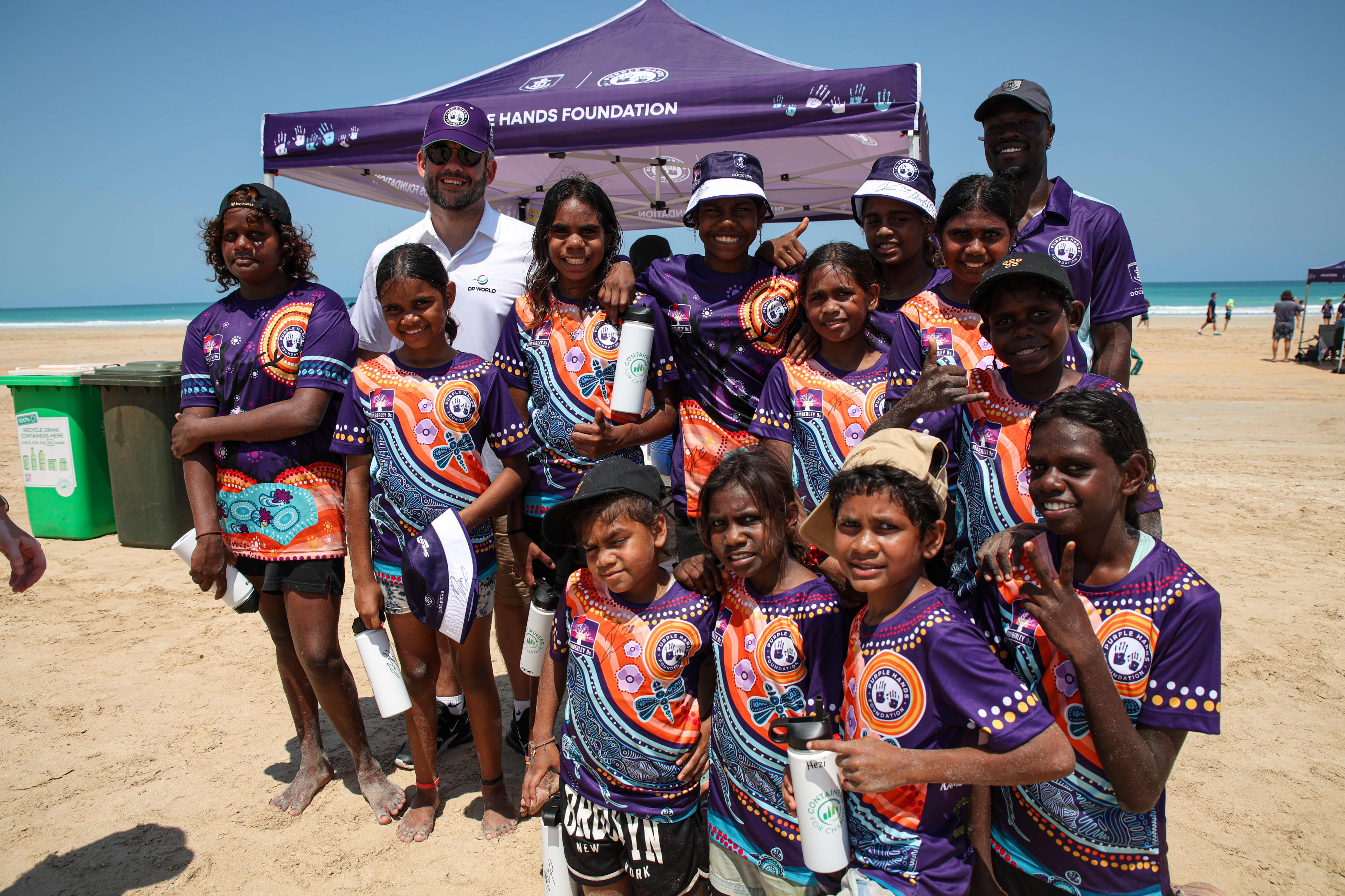 Students standing on beach in front of the Purple hands foundation tent