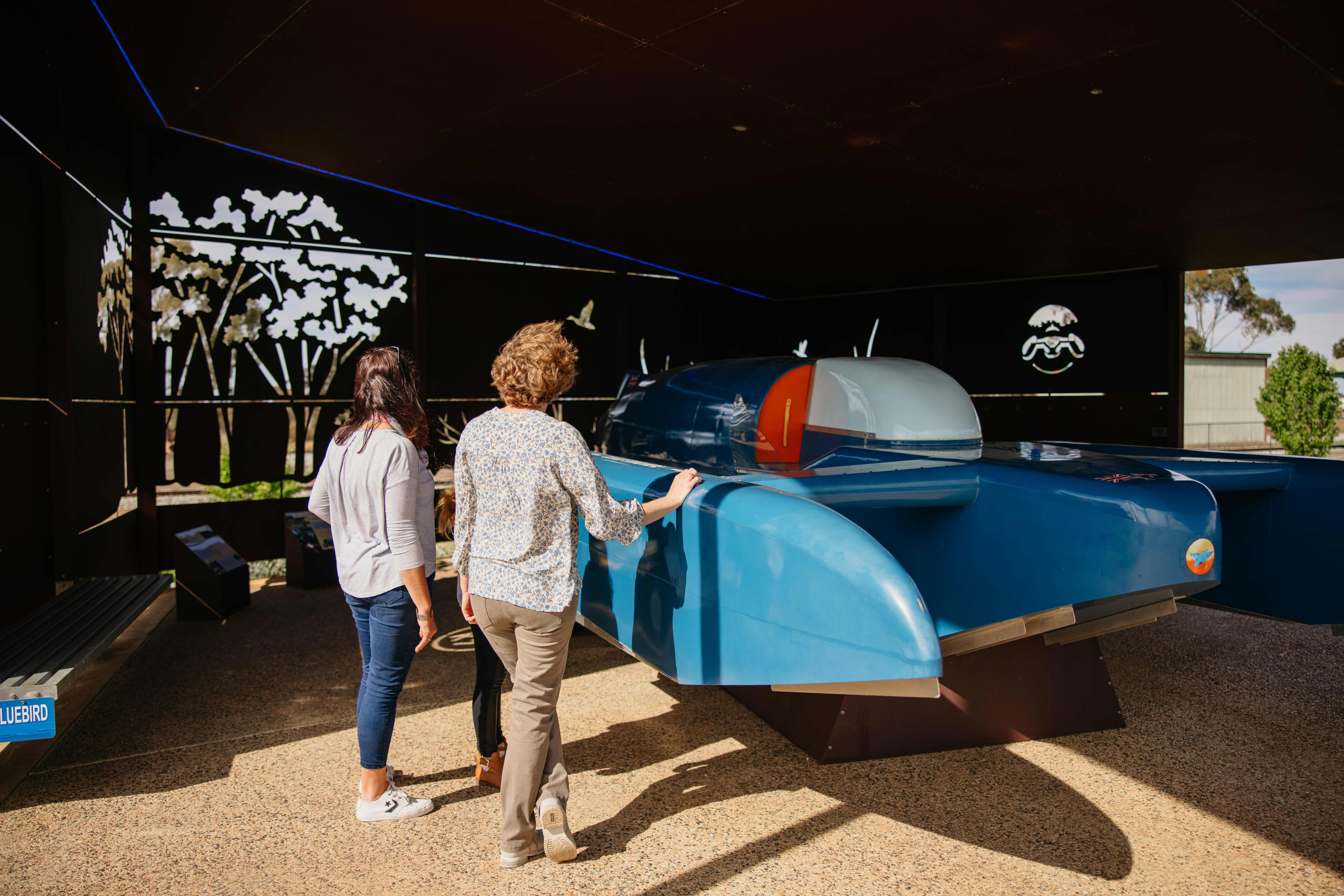 Two ladies observing a large blue replica of a jet propelled hydroplane boat.