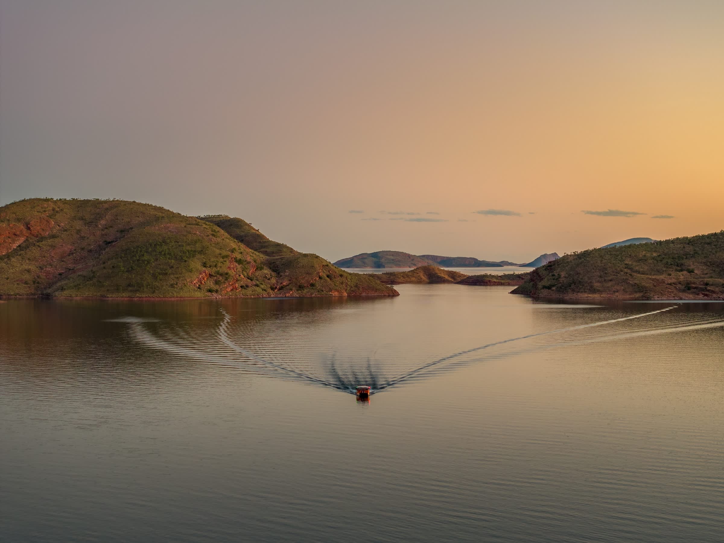 An aerial shot of a boat gliding along a river system, with surrounding rugged landscape.