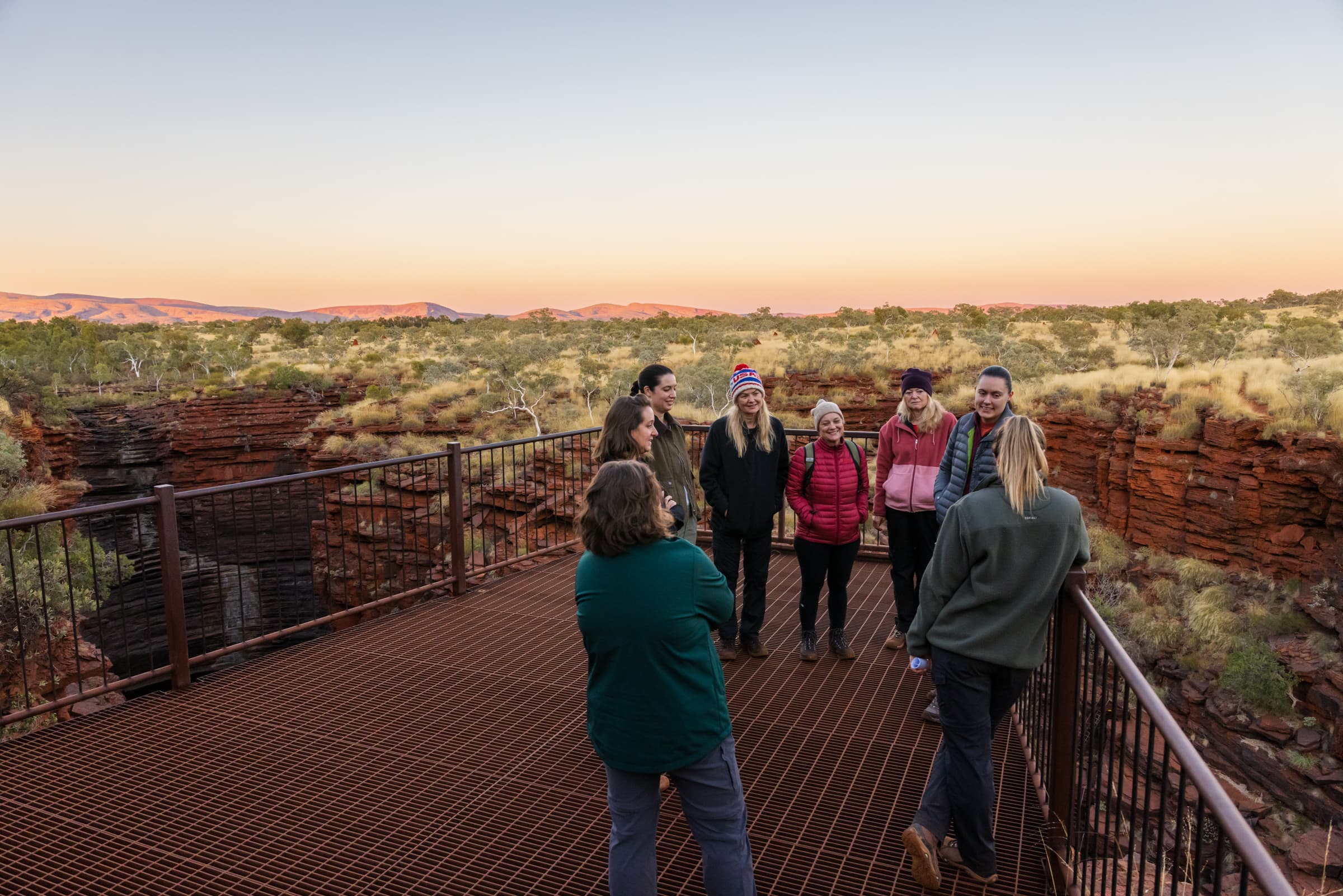 A steel lookout suspended over a deep-cut gorge, with 8 hikers smiling.