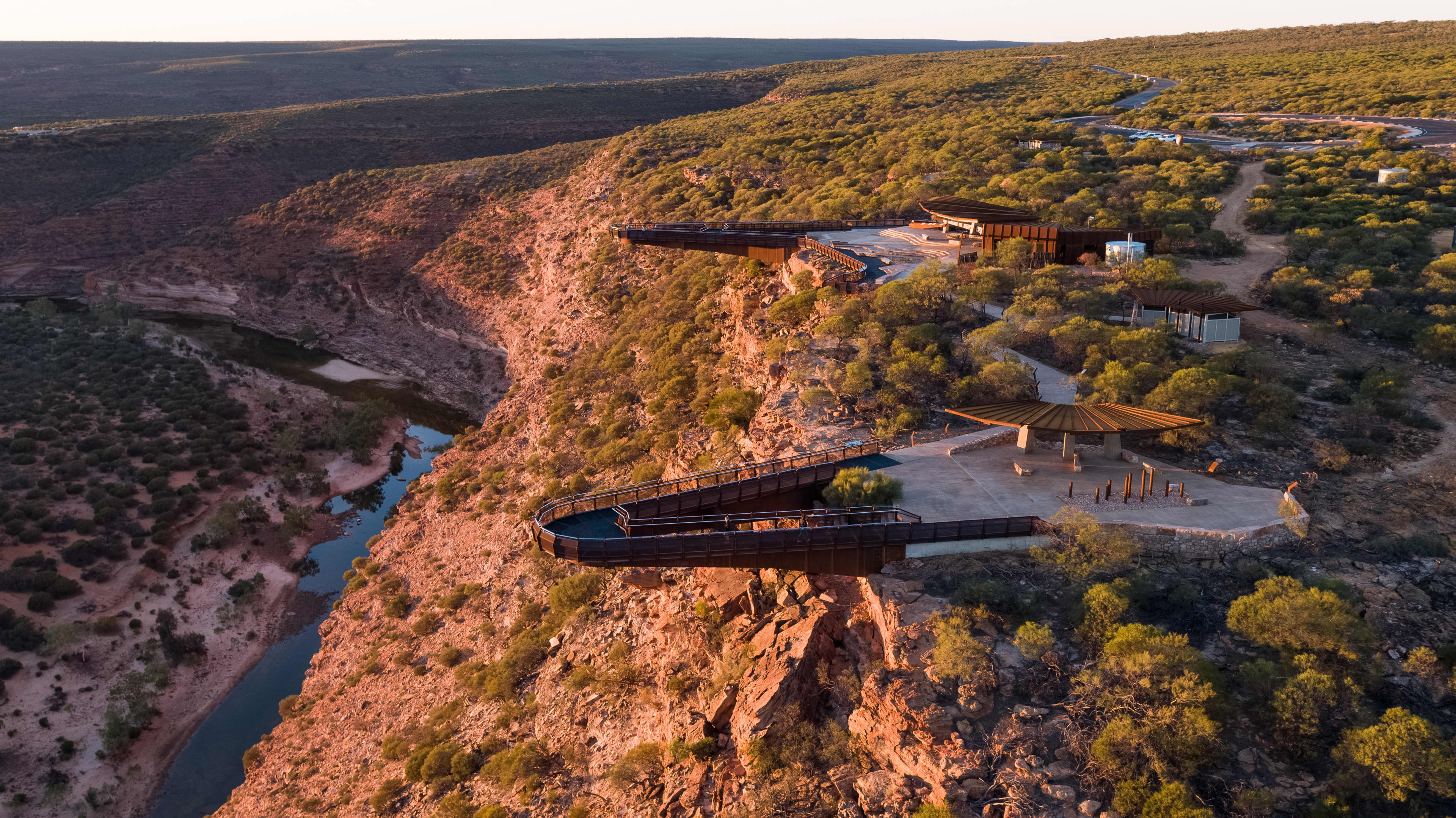 A large metal skywalk suspended above a winding river deep gorge.