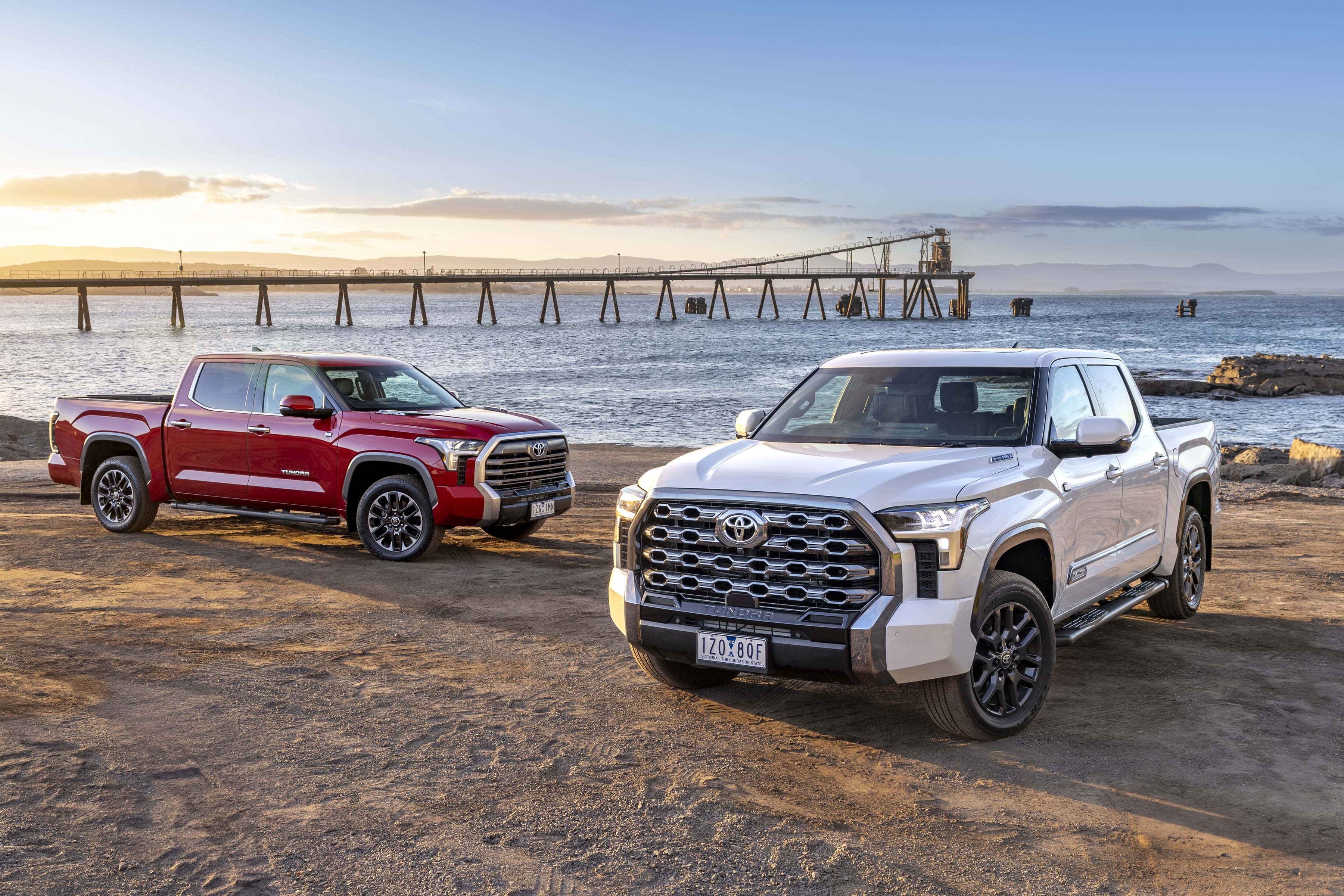 Two Toyota Tundra hybrid utes parked near a beach