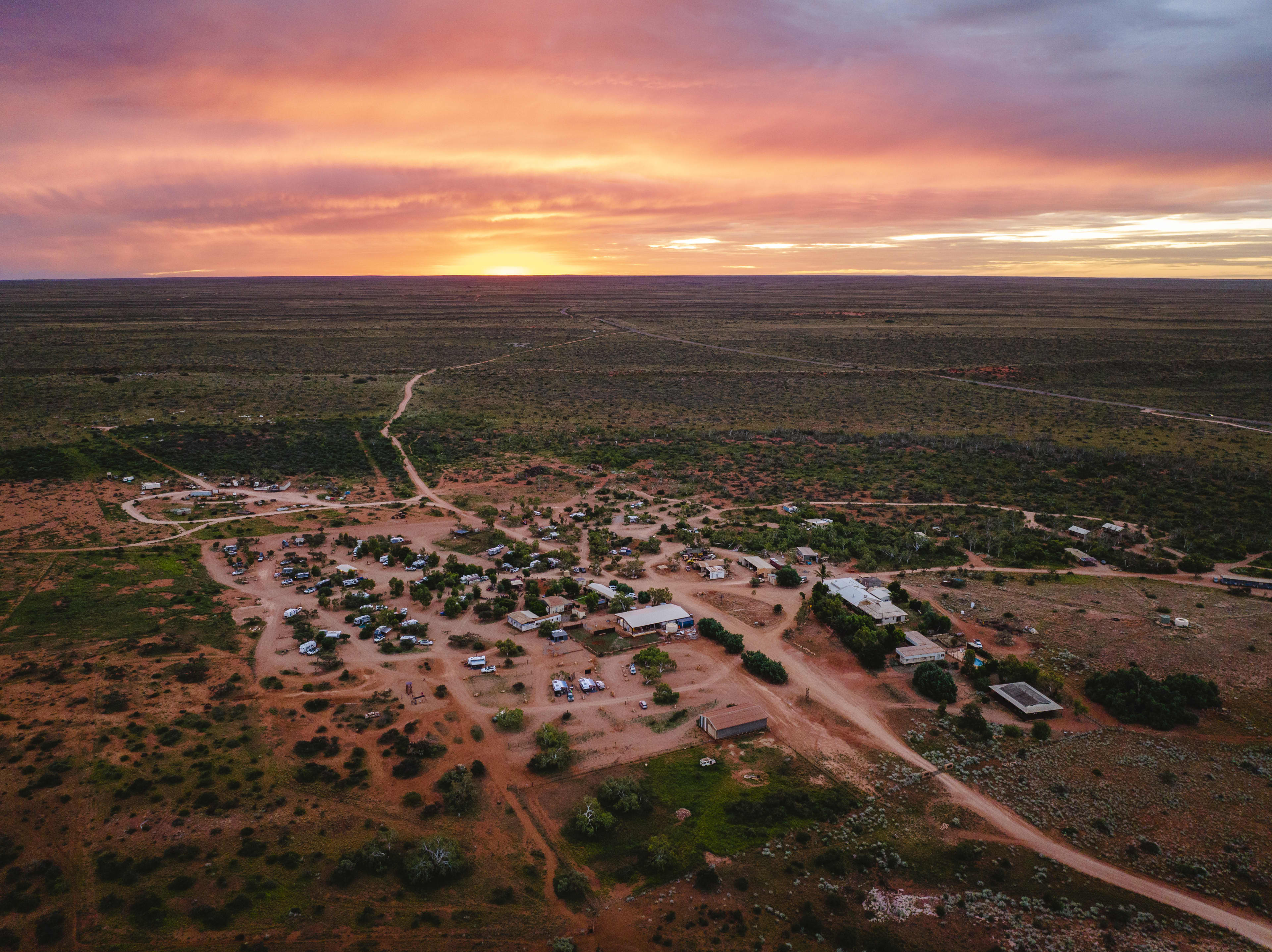 An aerial image with sunset skies over a large red dirt caravan park.