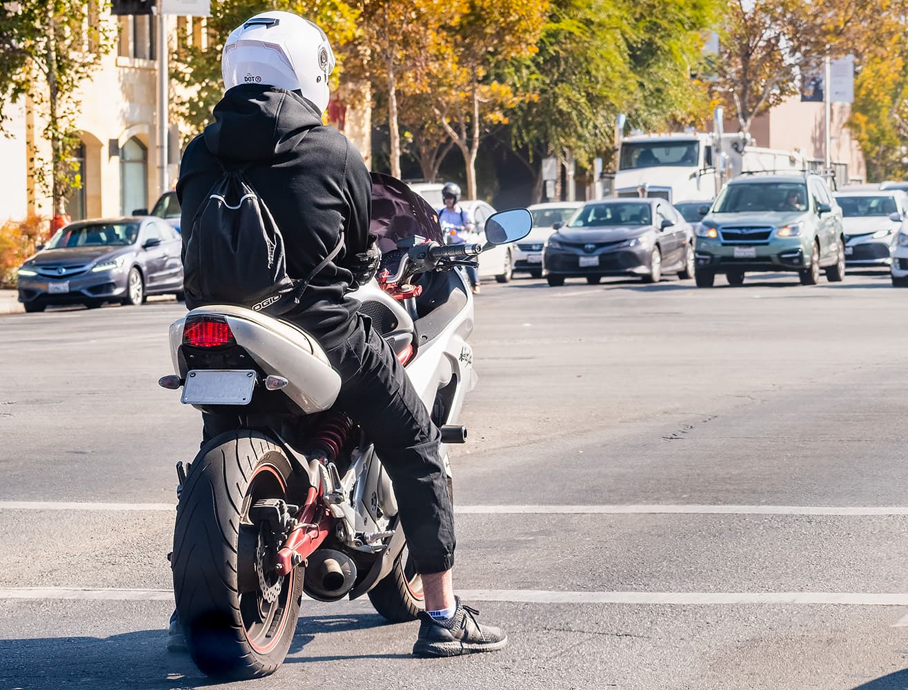 A motorcycle rider waiting at a stop line in traffic.