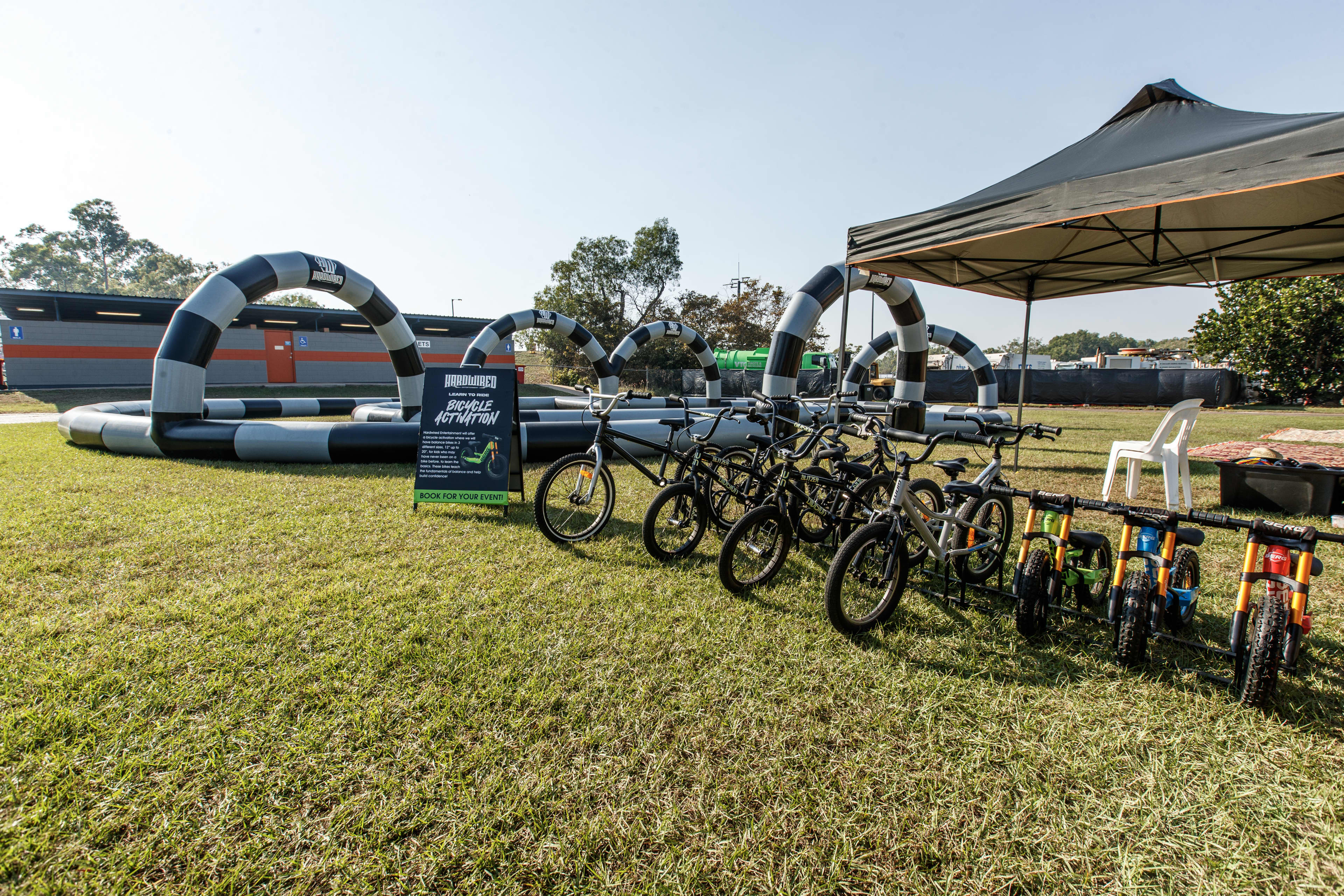 A large grass lawn with a row of adults and kids' bikes, with a blow-up inflatable course in the background.