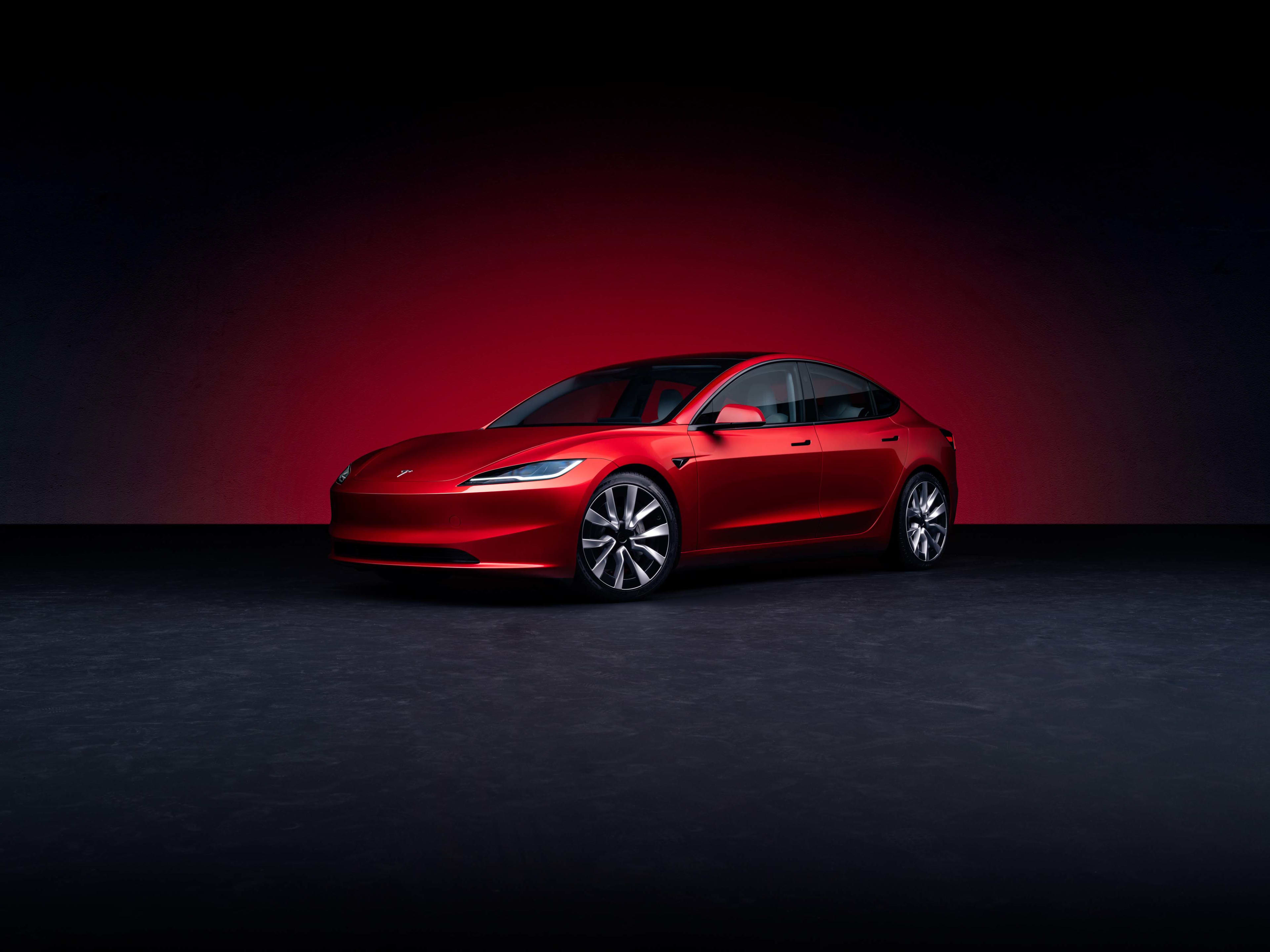 A red Tesla model 3 in a dark studio setting