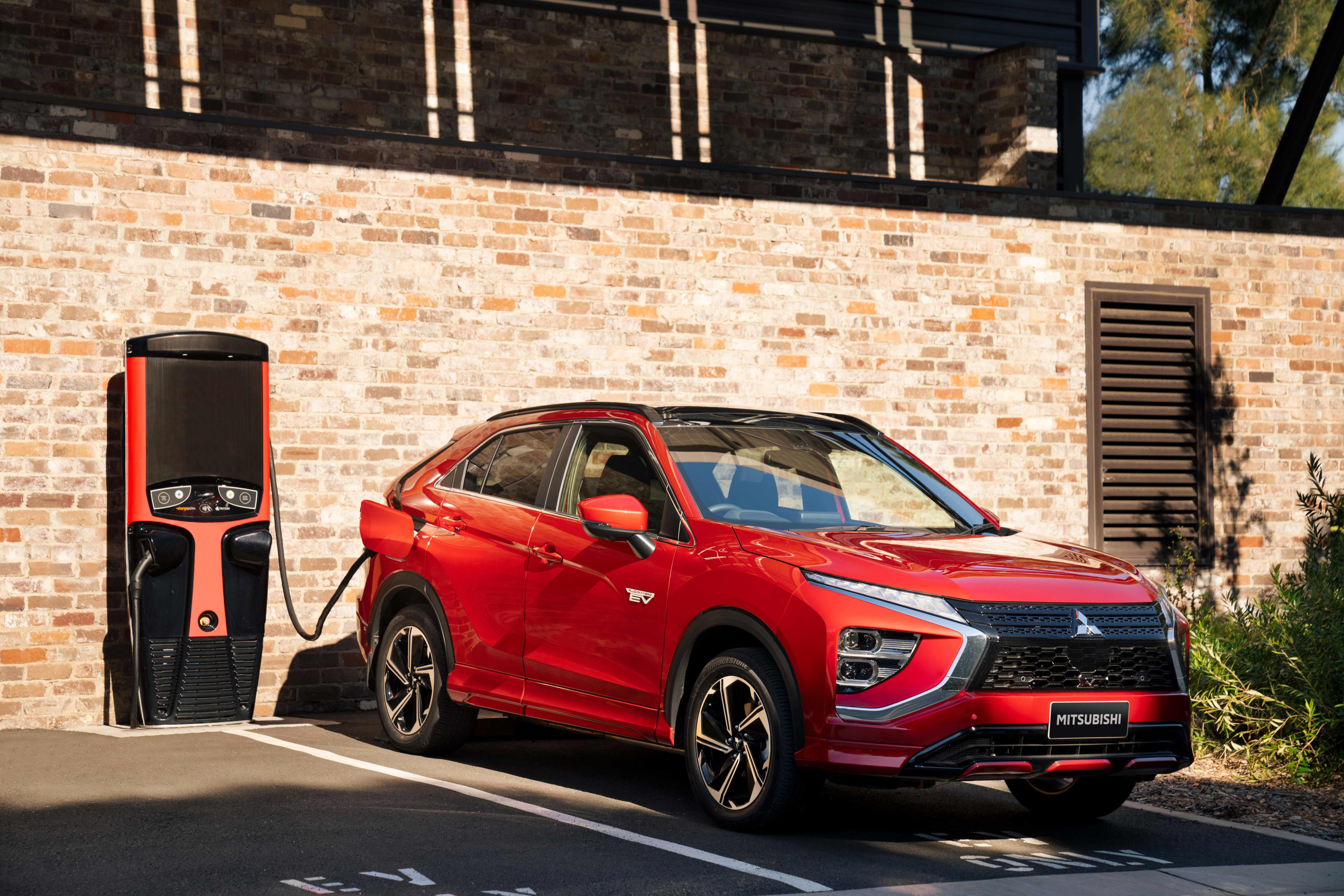 A red Mitsubishi Eclipse Cross PHEV parked near a red brick wall