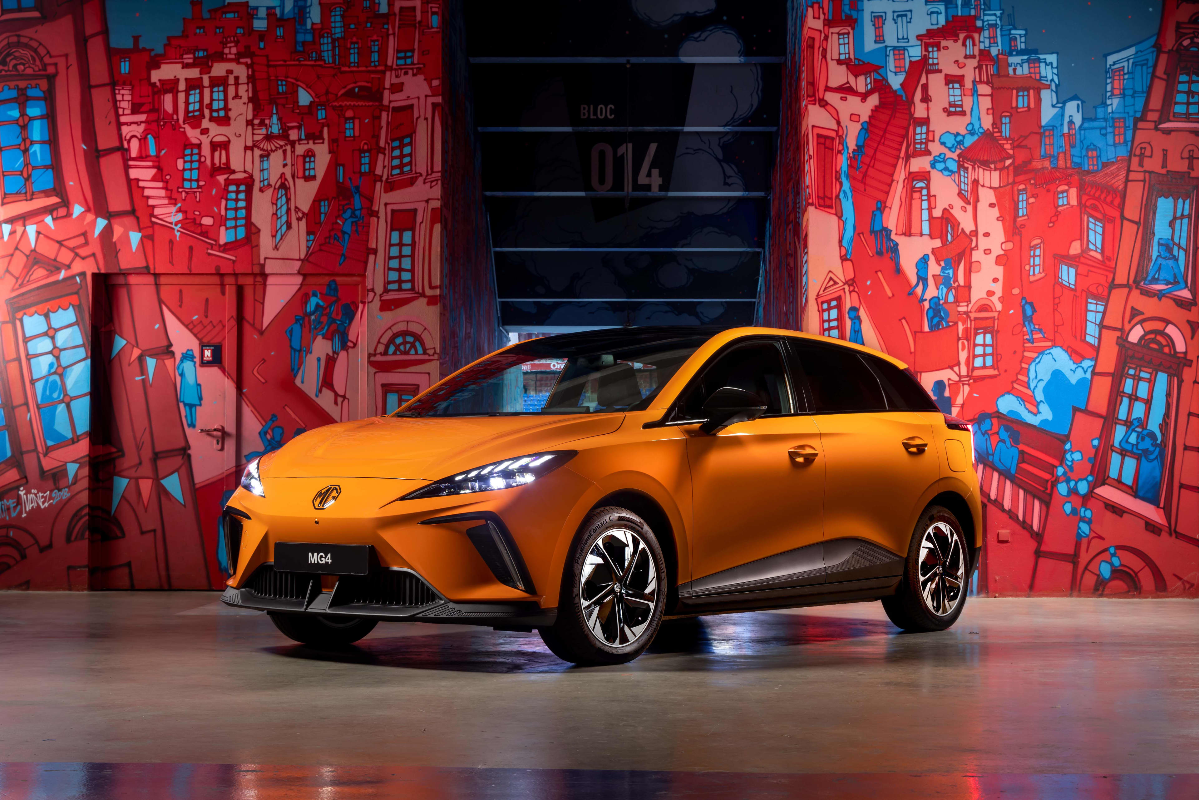 An orange MG4 near a wall with a  bright mural