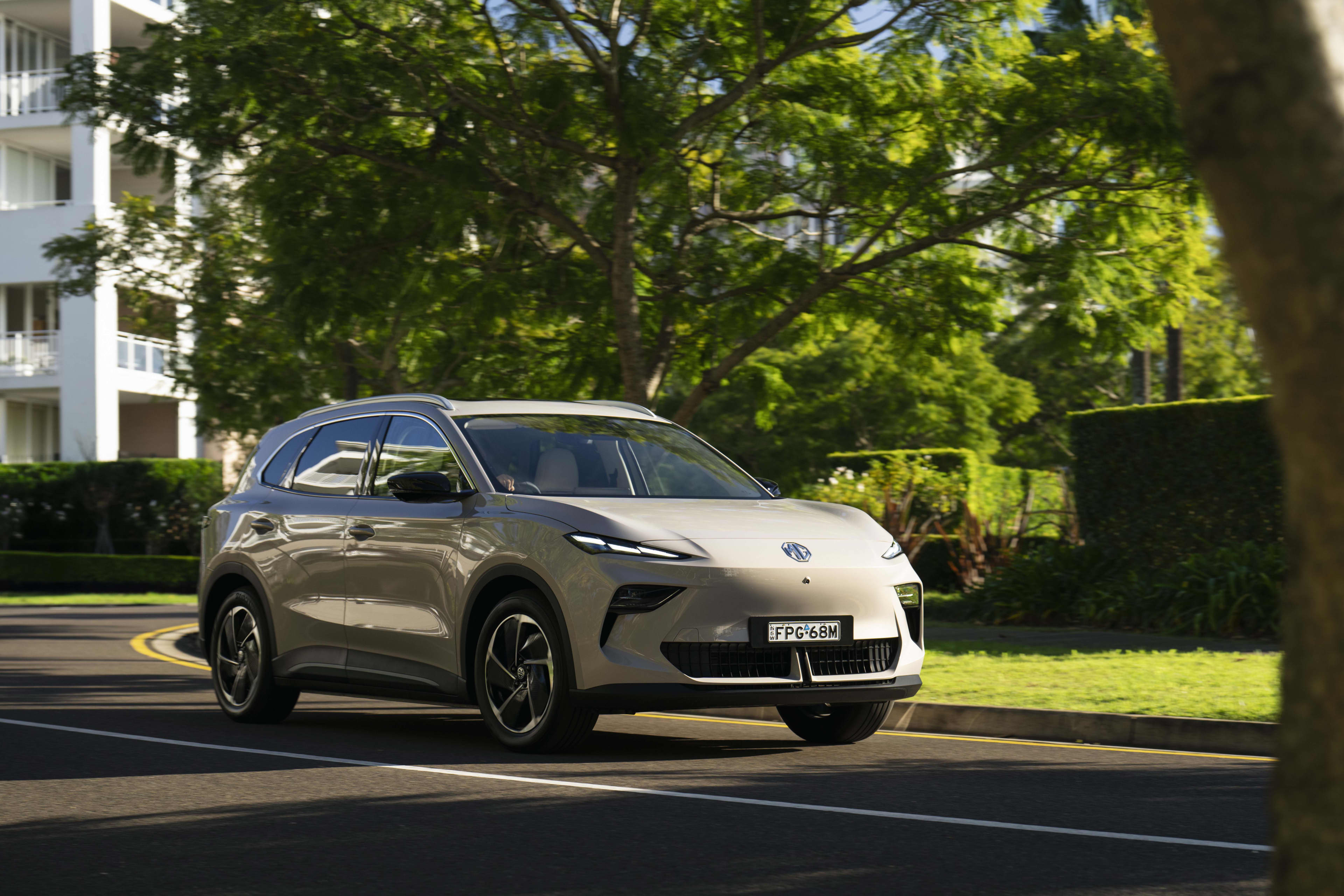 A light brown MG s5 driving near a city park near apartments