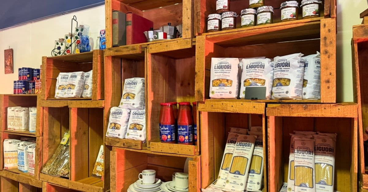 Pantry of Italian items like passata and pasta in wooden shelves.