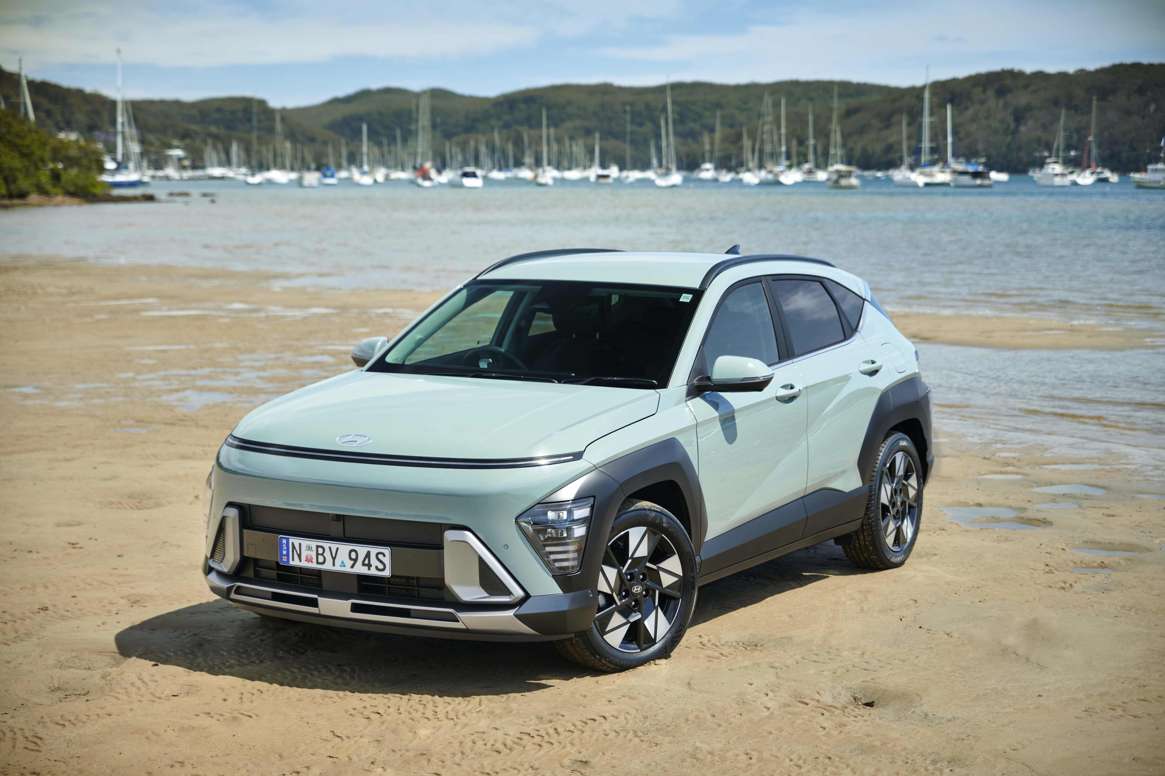 A light green Hyundai Kona hybrid parked on a river shoreline