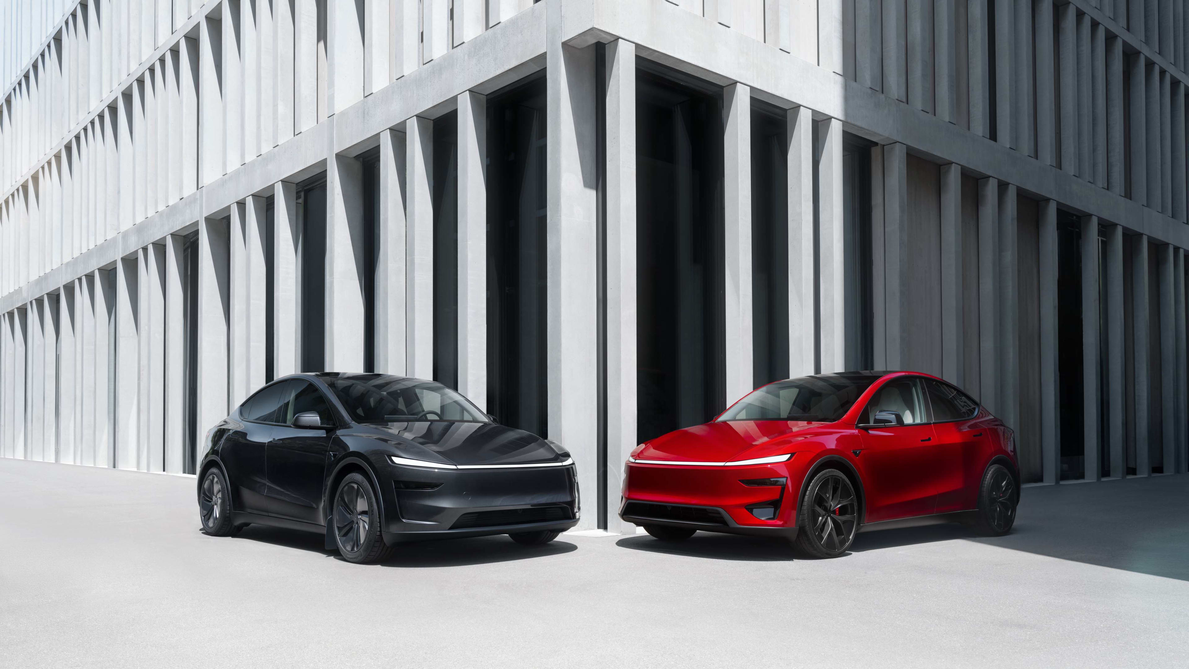 A black and a red Tesla model Y EVs parked in front of a modern building