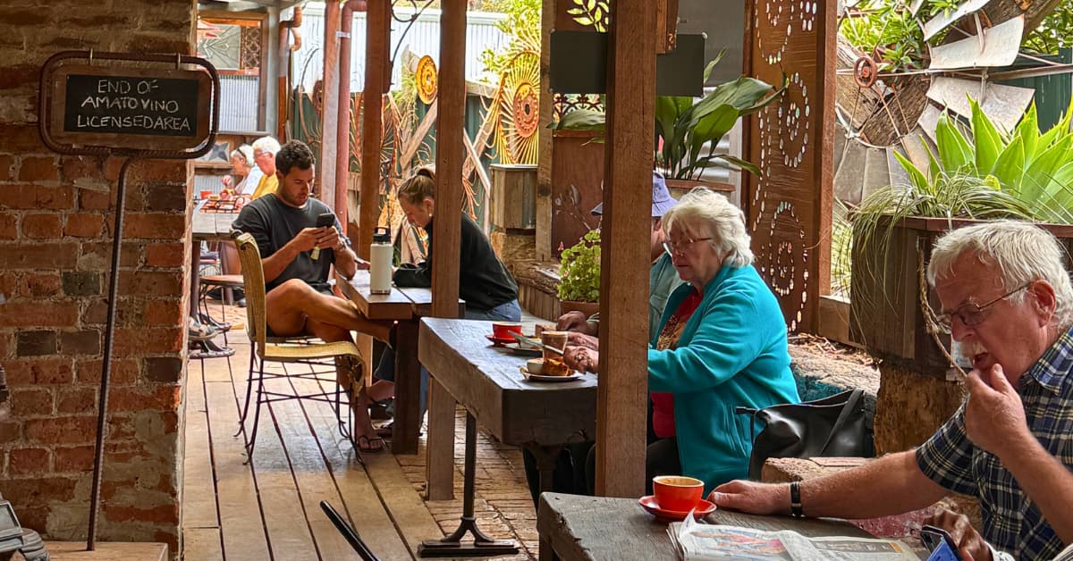 People enjoying coffee and food outdoors of cafe in garden filled with ornaments