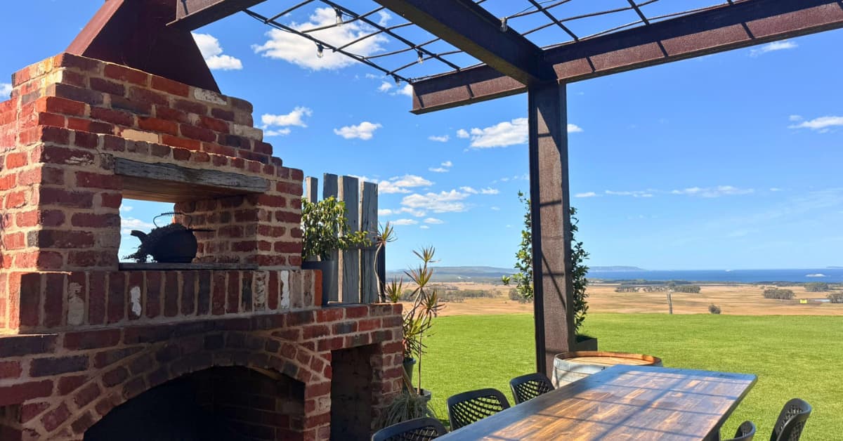Old brick outdoor fireplace with cafe seating and views of green lawn and ocean in distance