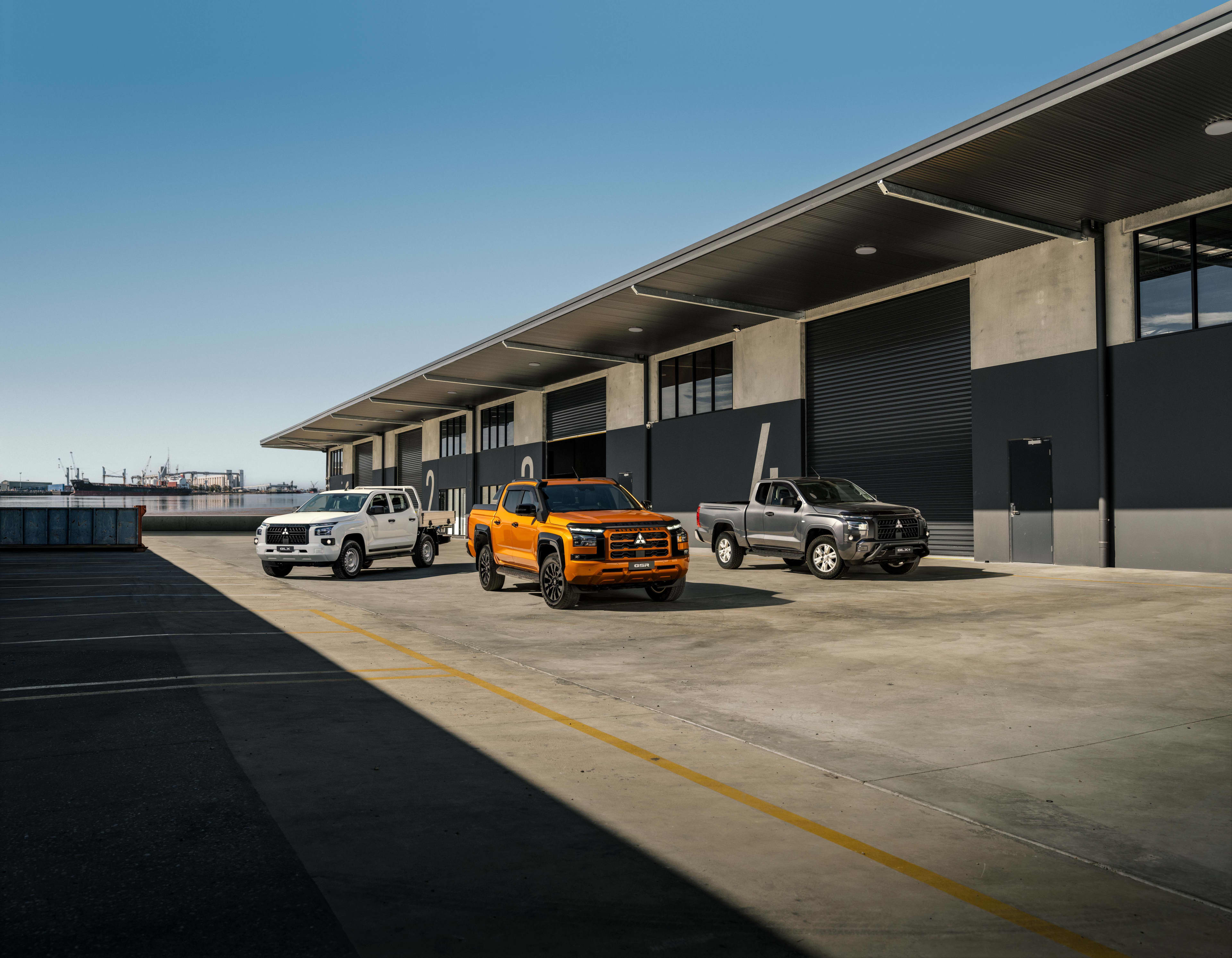 Three Mitsubishi Triton utes parked in front of a commercial building