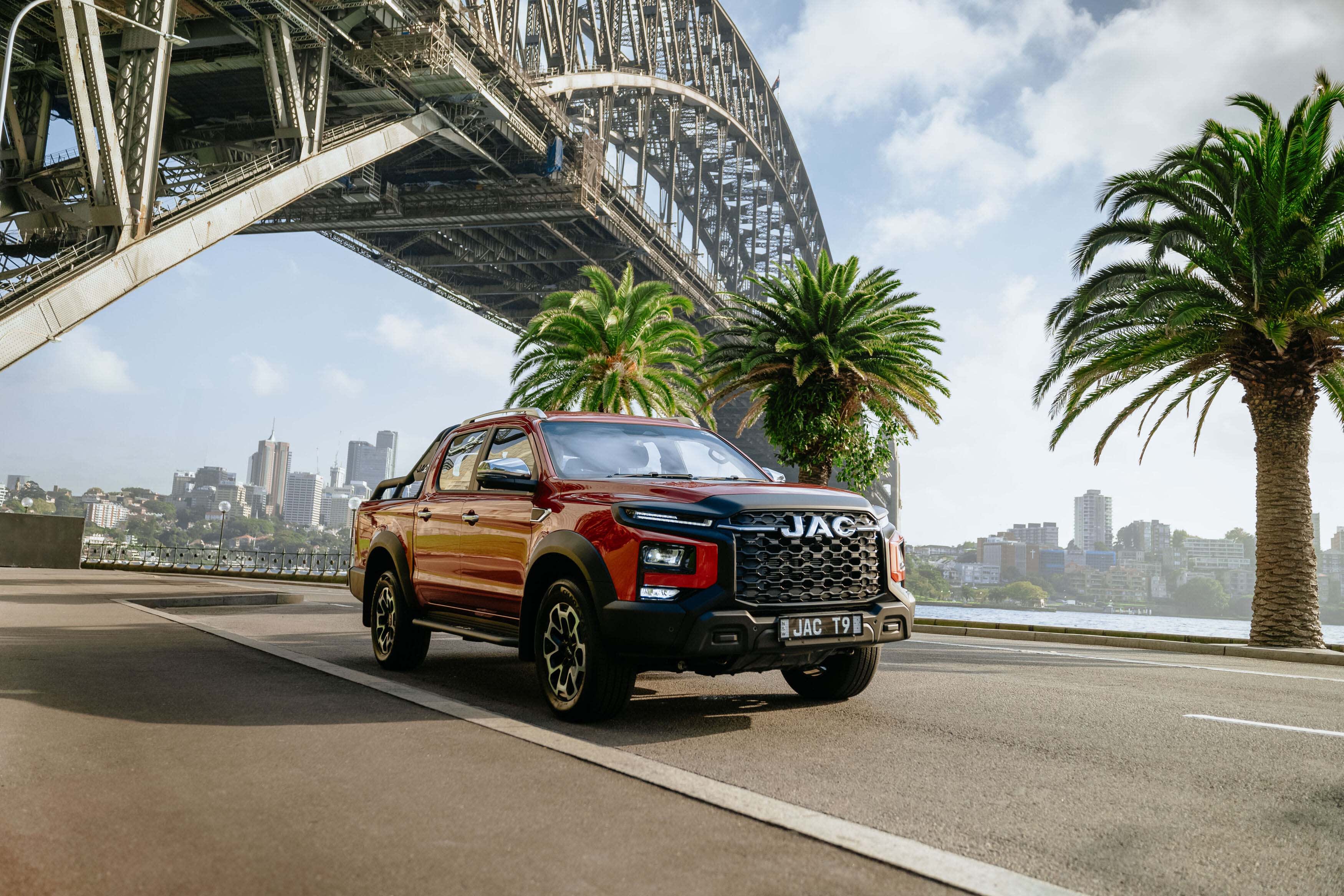A red JAC T9 ute driving under a bridge