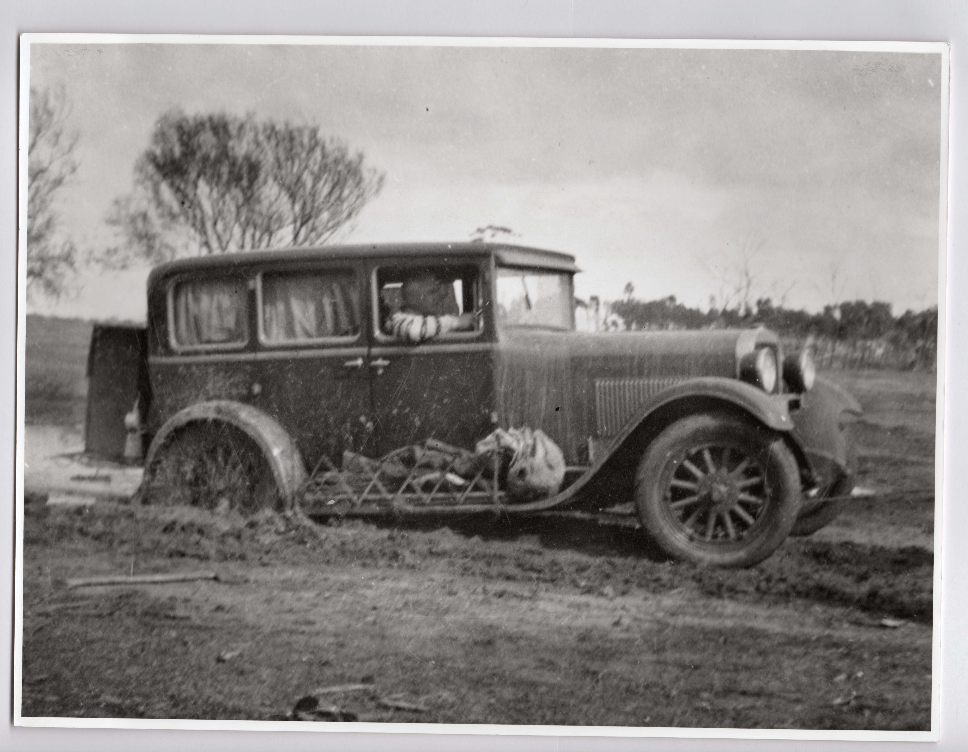 A black and white image of a vintage car driving through deep mud