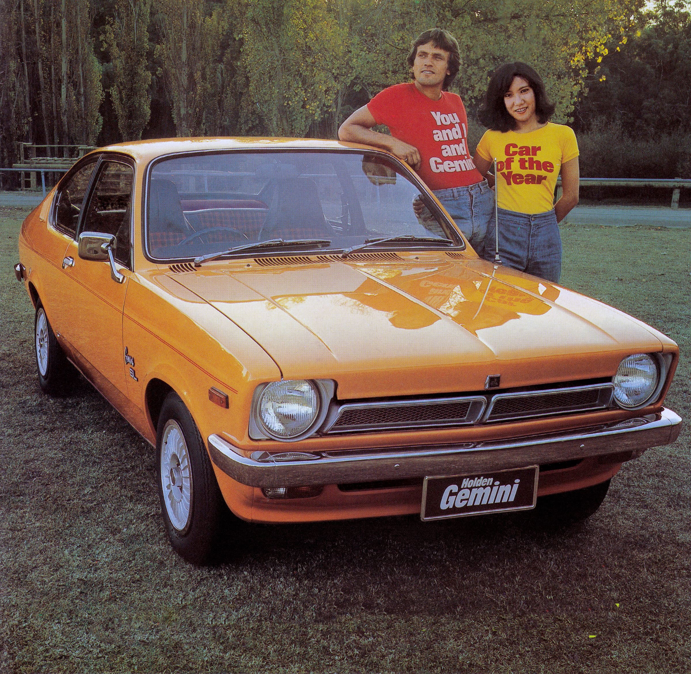 Two people next to an orange 1976 Holden Gemini