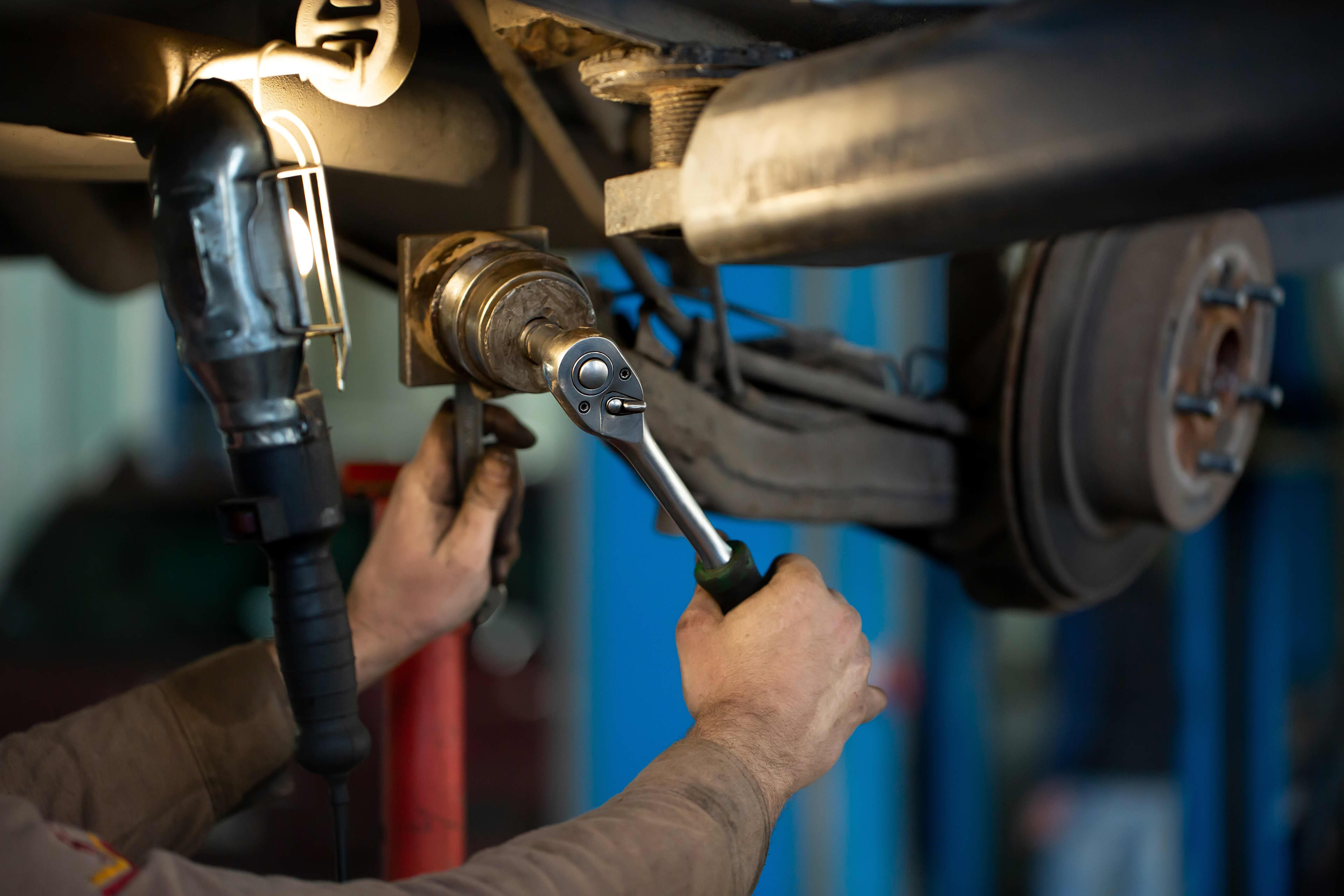 A close-up of a person's arm with a tool working under a car on a hoist