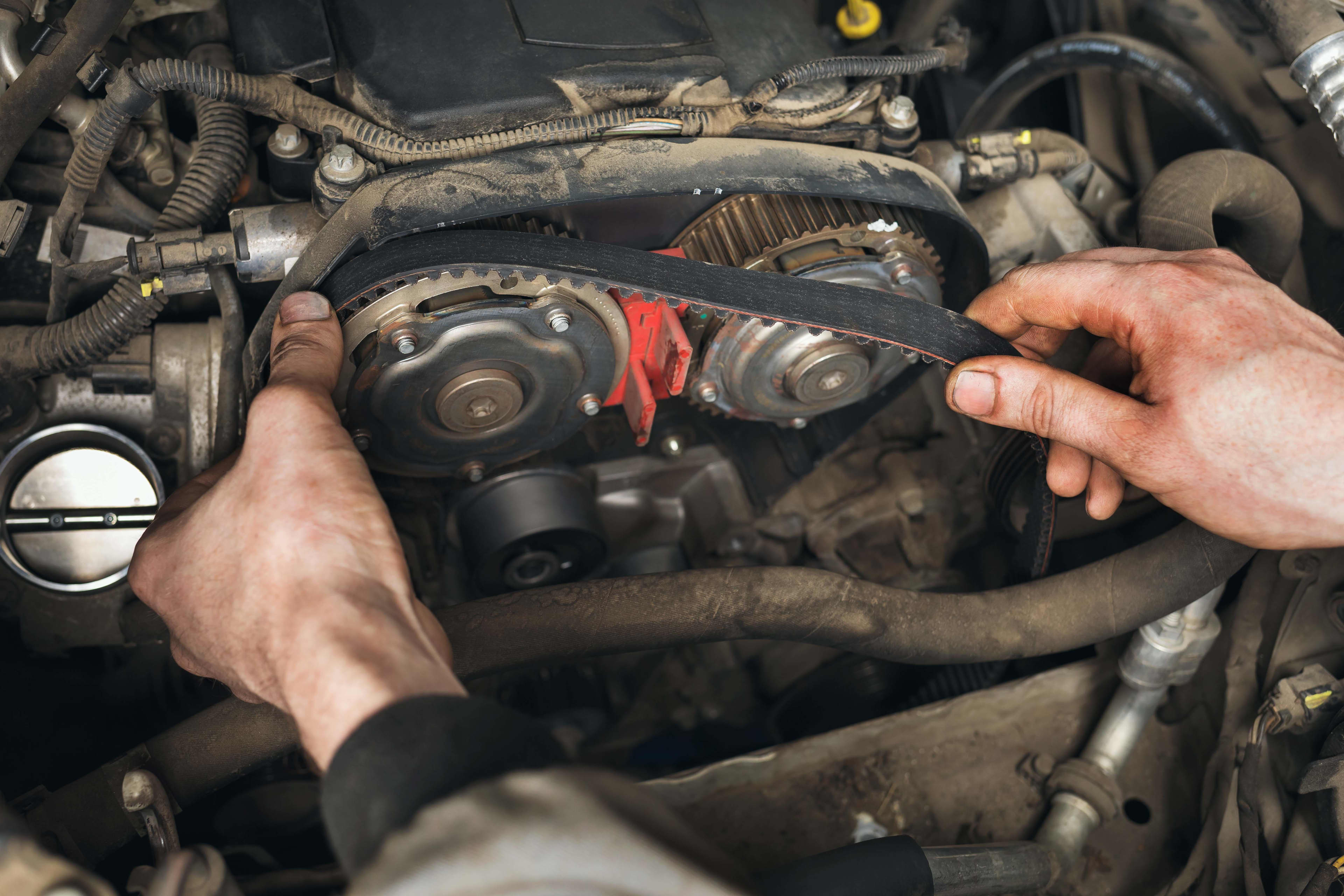 A person is fitting a timing belt to a car