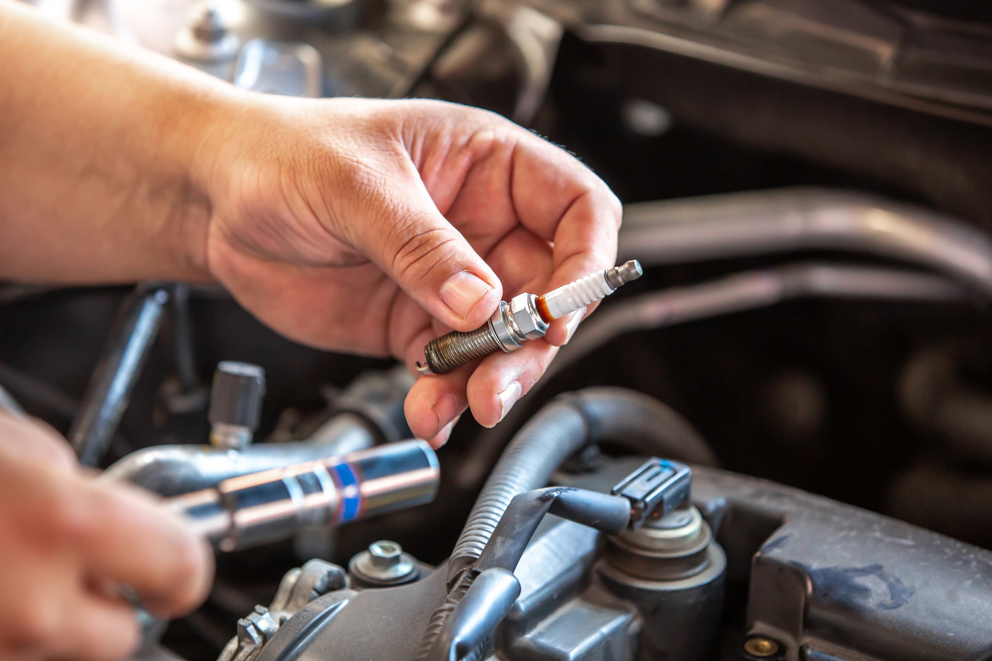 A person holds an automotive sparkplug over a car engine