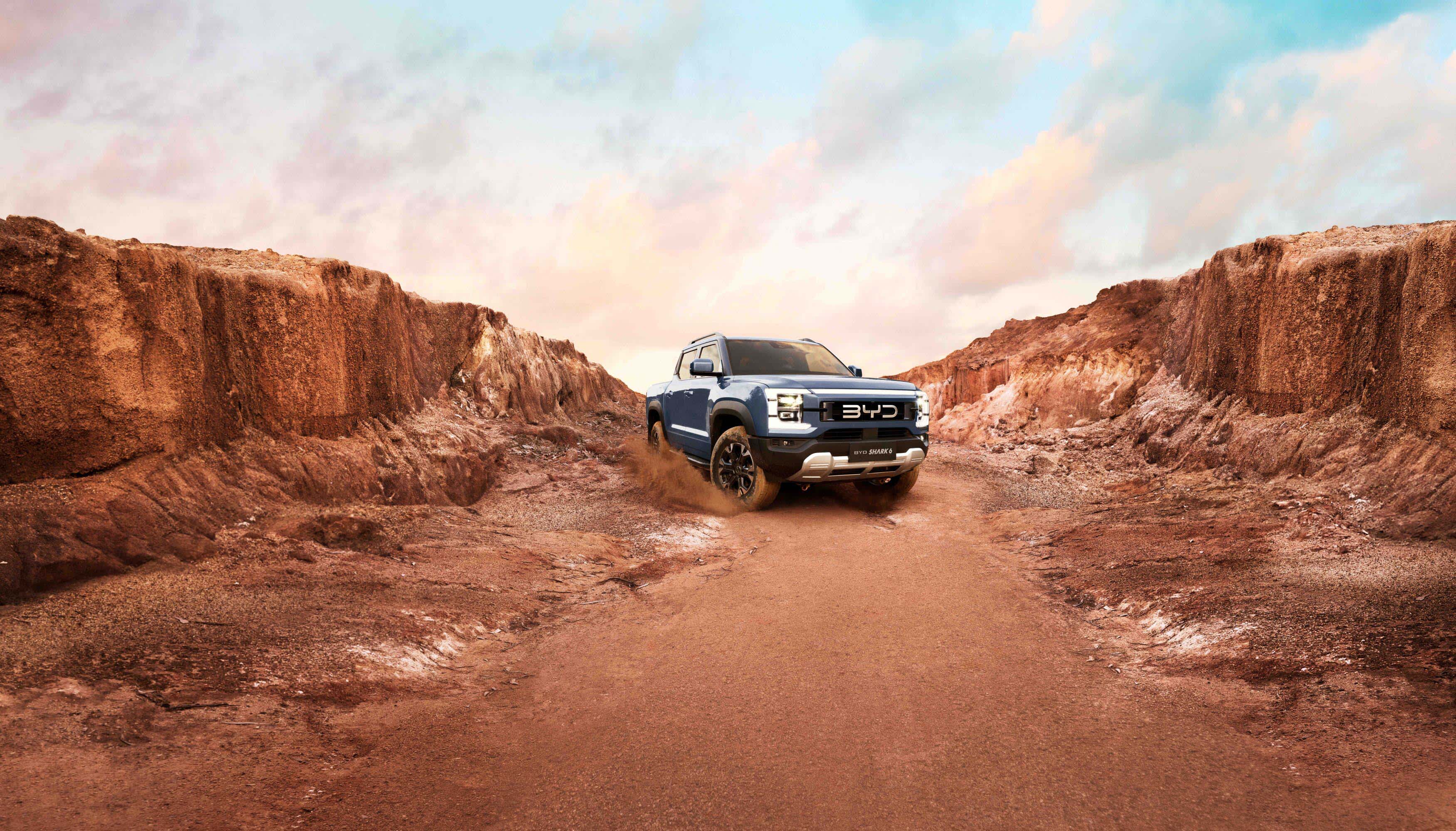 A BYD SHARK 6 PHEV ute driving between red dirt hillsides