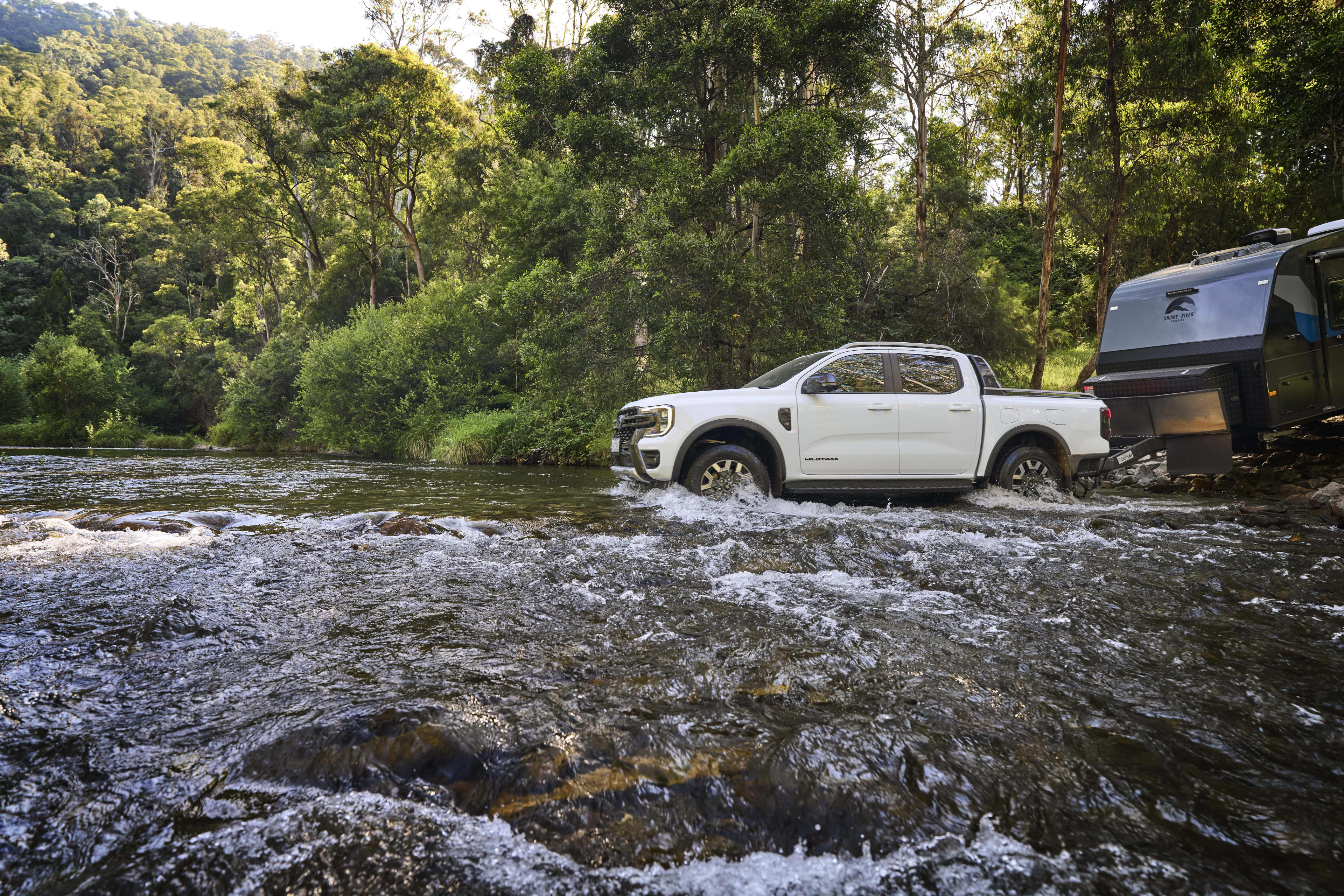 A white Ford Ranger PHEV ute towing a caravan across a flowing waterway