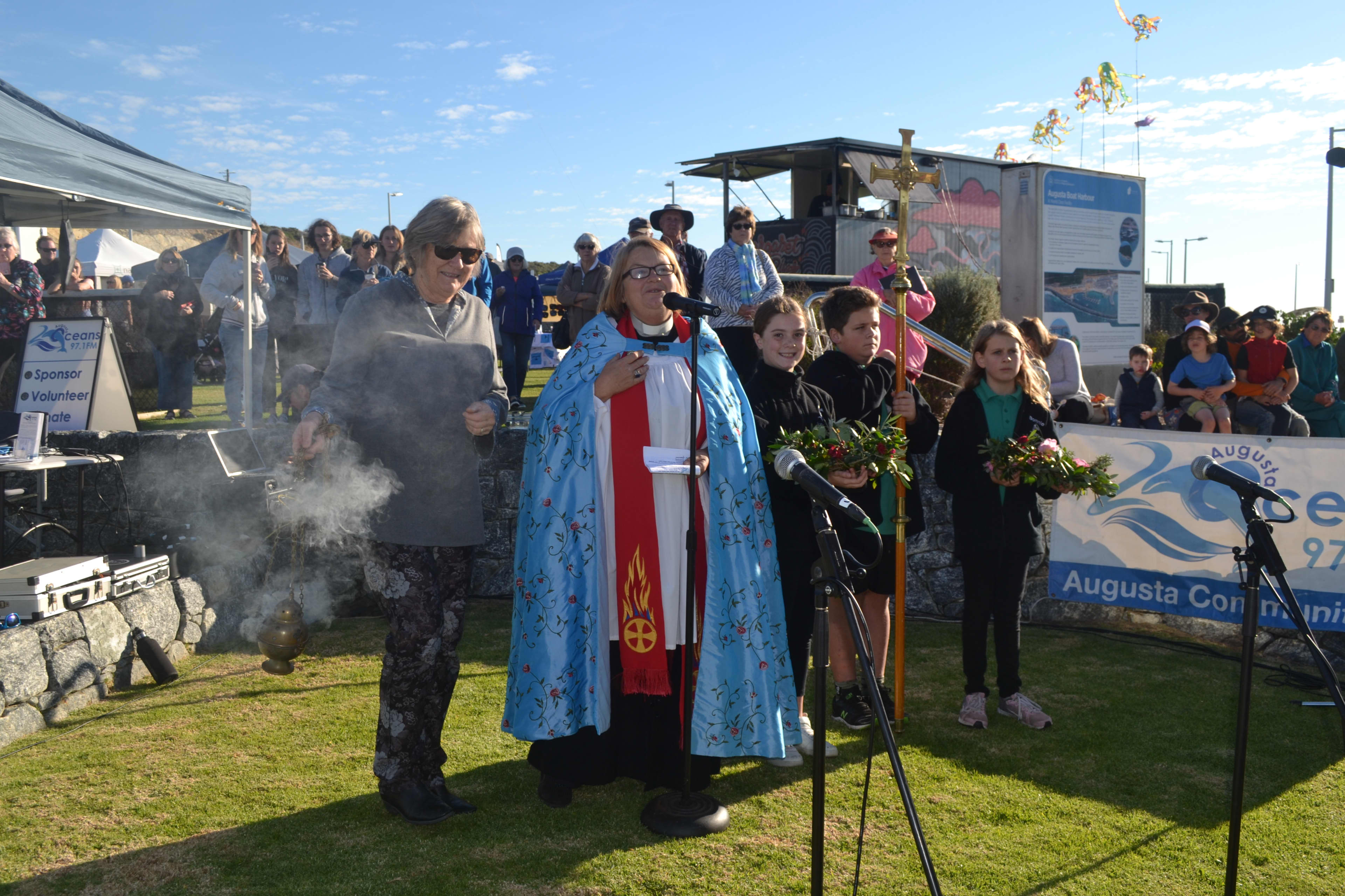 Welcome to Country at event with children and community members and microphones outdoors on grass.